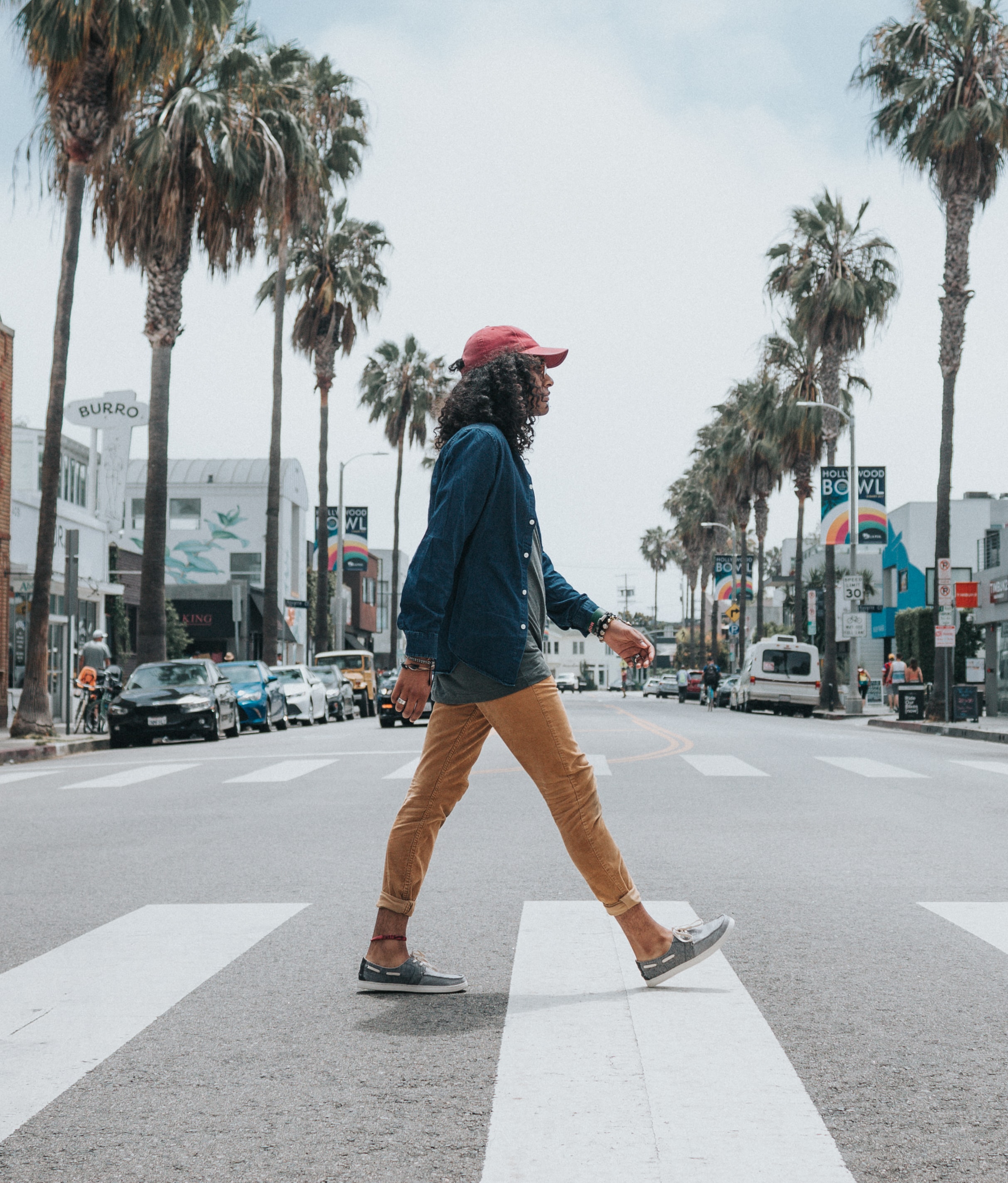 Man in a red hat walking in the crosswalk with palm trees in the background.