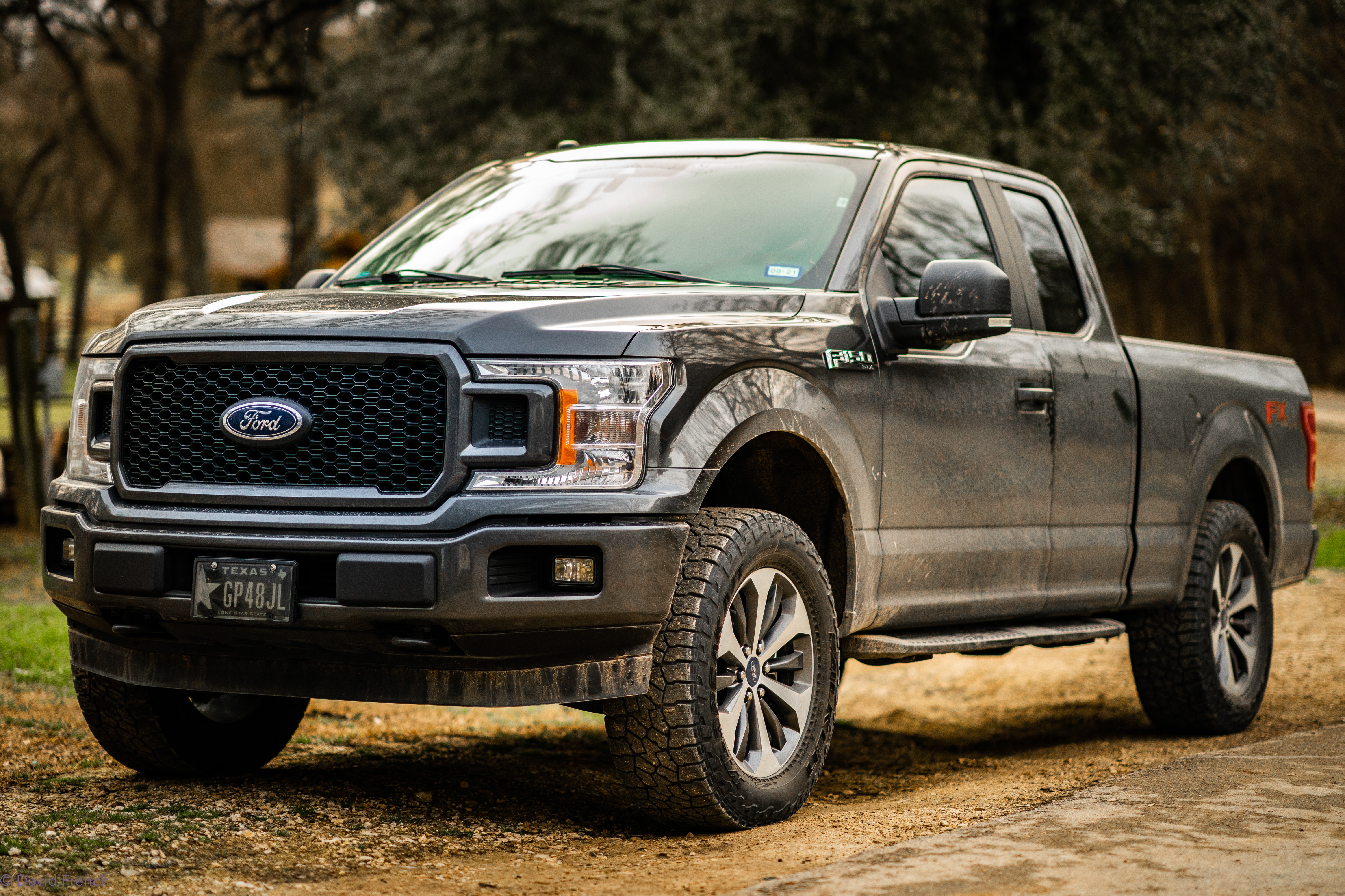 Ford truck on a dirt road with trees.