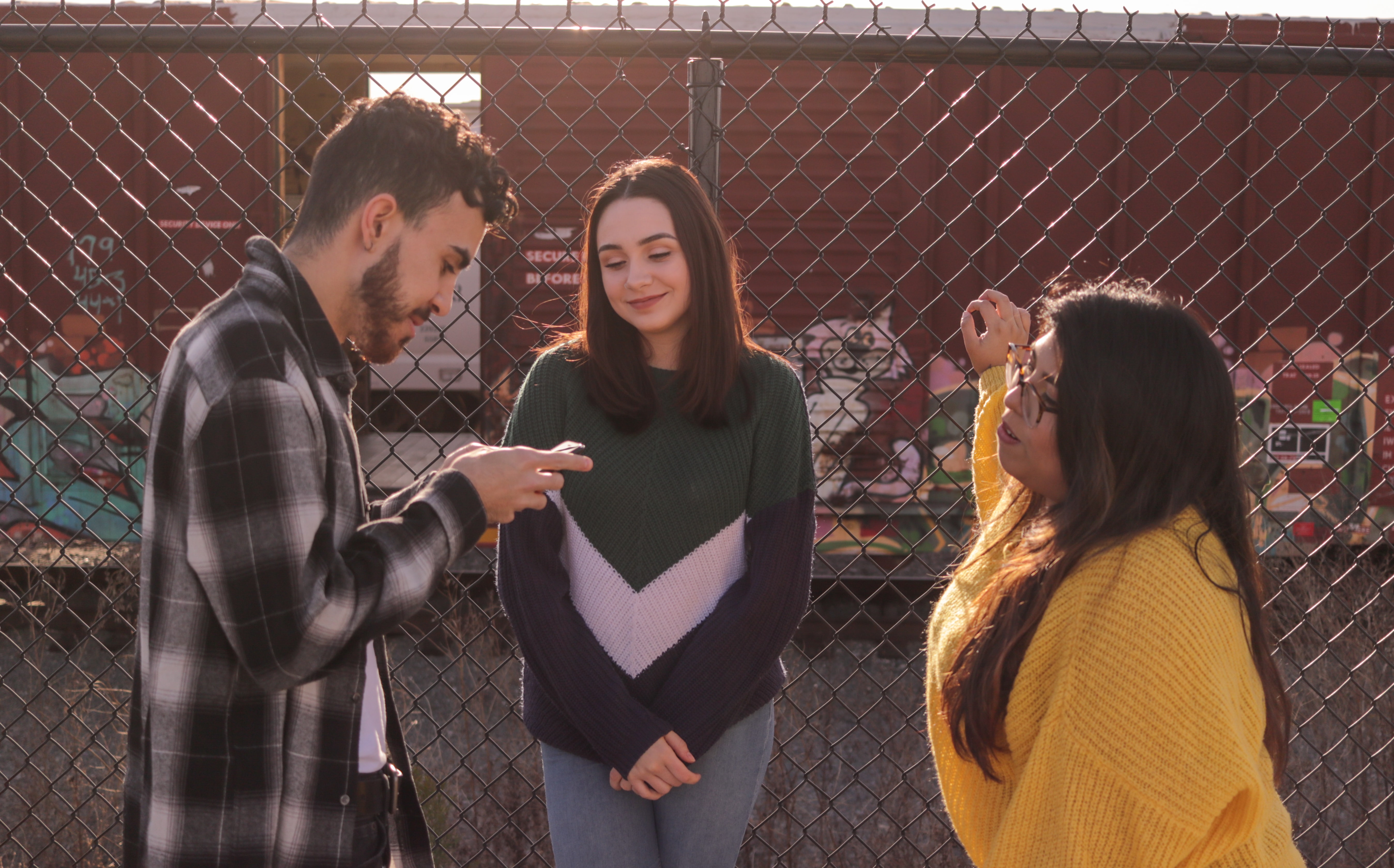 Man looking on his phone with two women looking on.