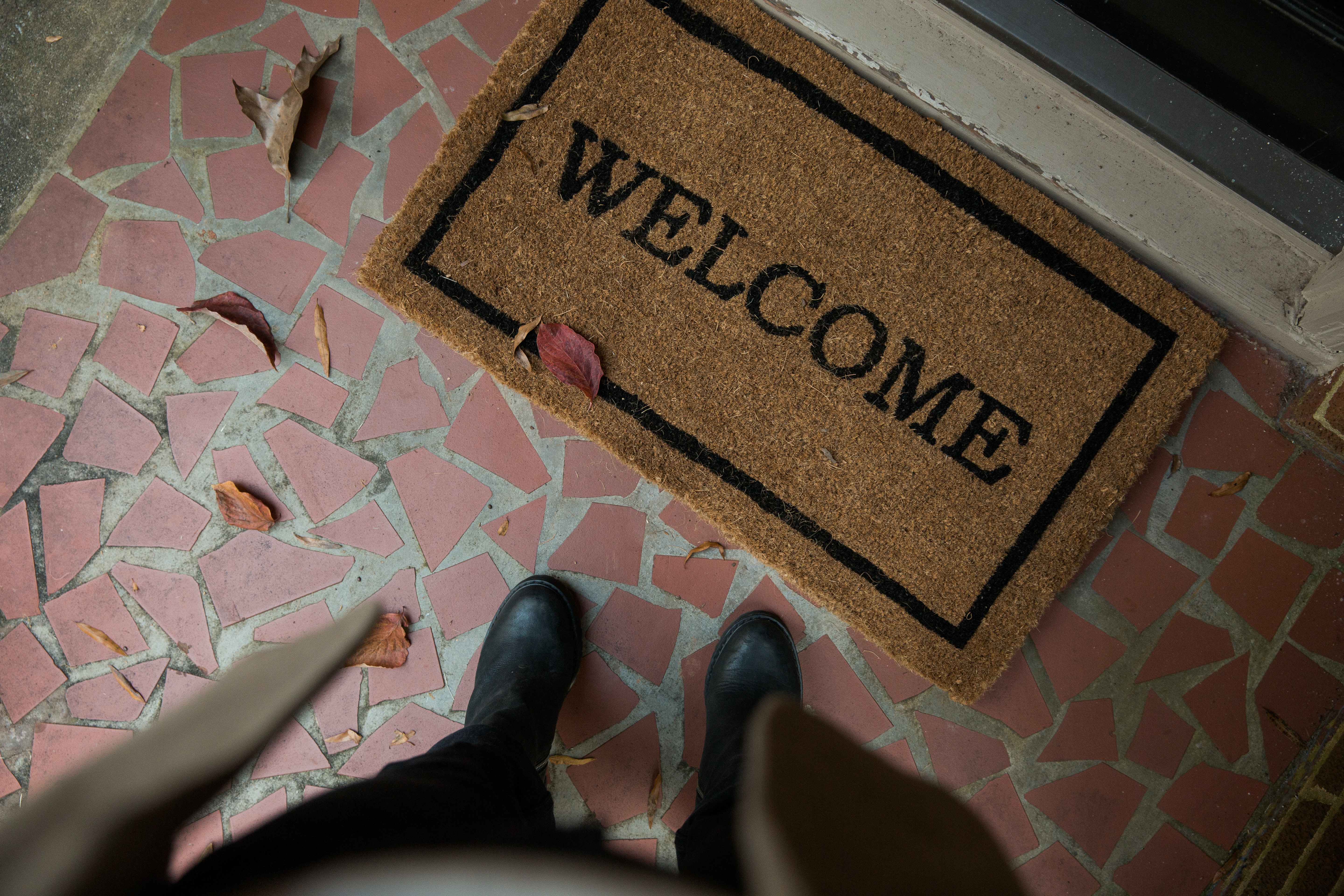 Man in trench coat waiting at the front door at a welcome mat.