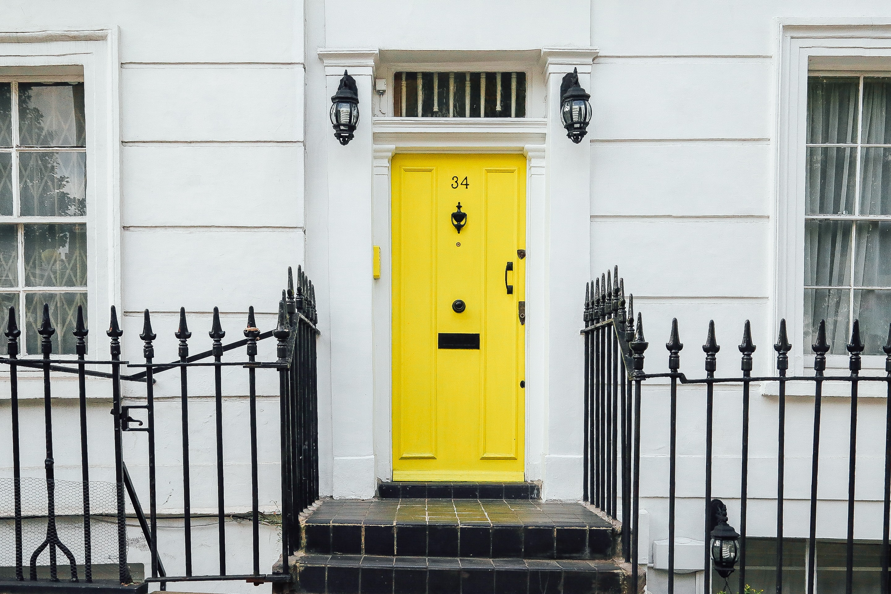 Yellow front door of a white home with a metal fence.