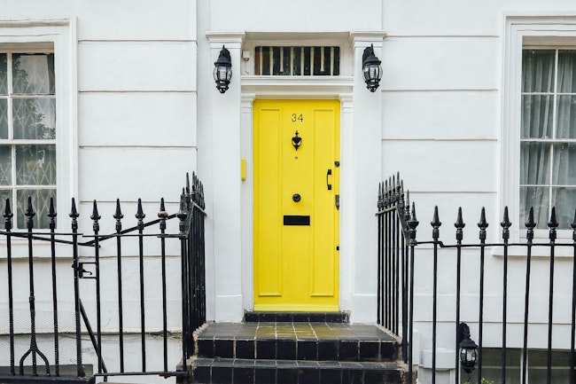 Yellow front door of a white home with a metal fence.