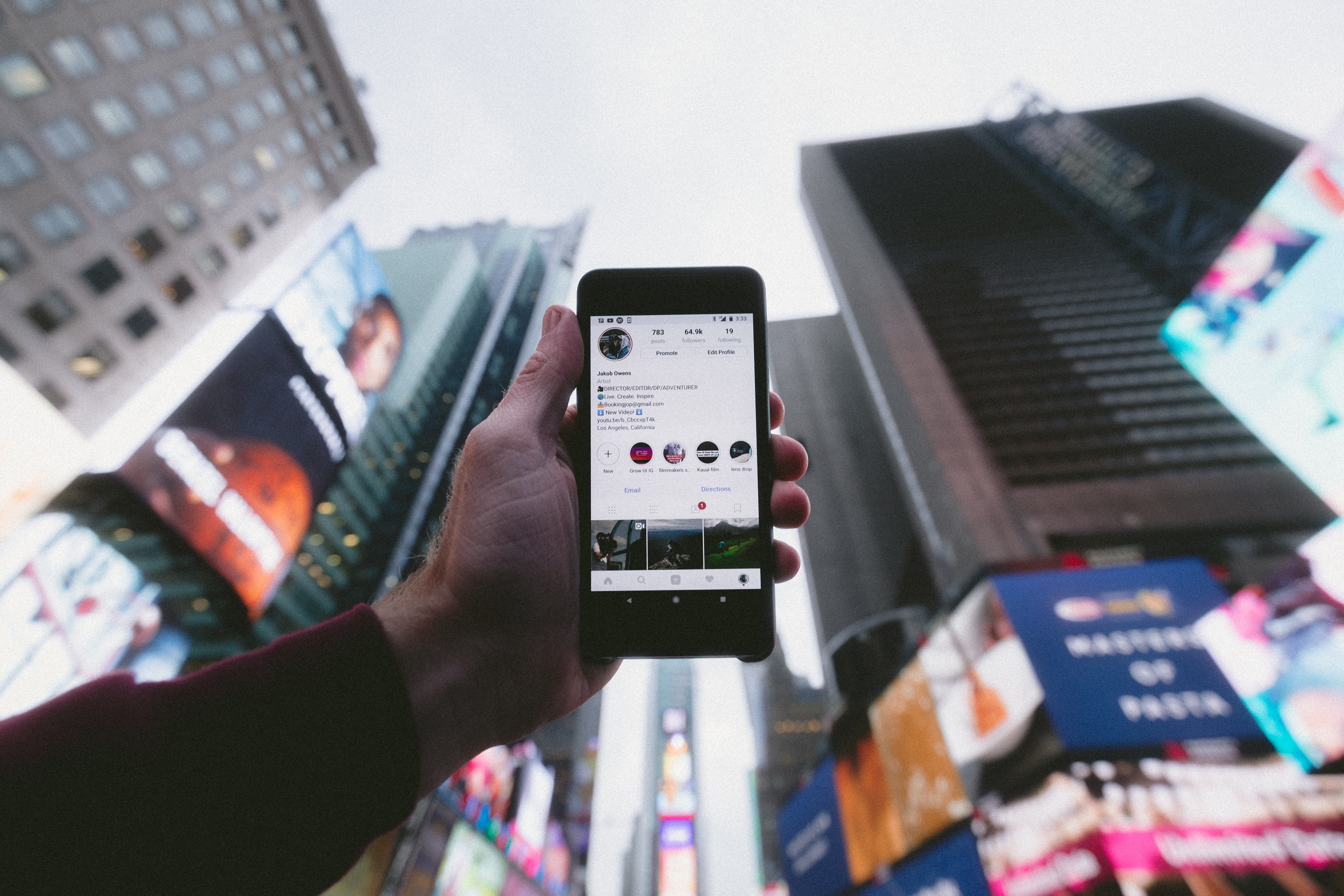 Person holding a smart phone up taking a photo and posting to social media of their travels to a big city.