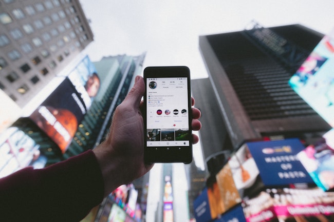 Person holding a smart phone up taking a photo and posting to social media of their travels to a big city.