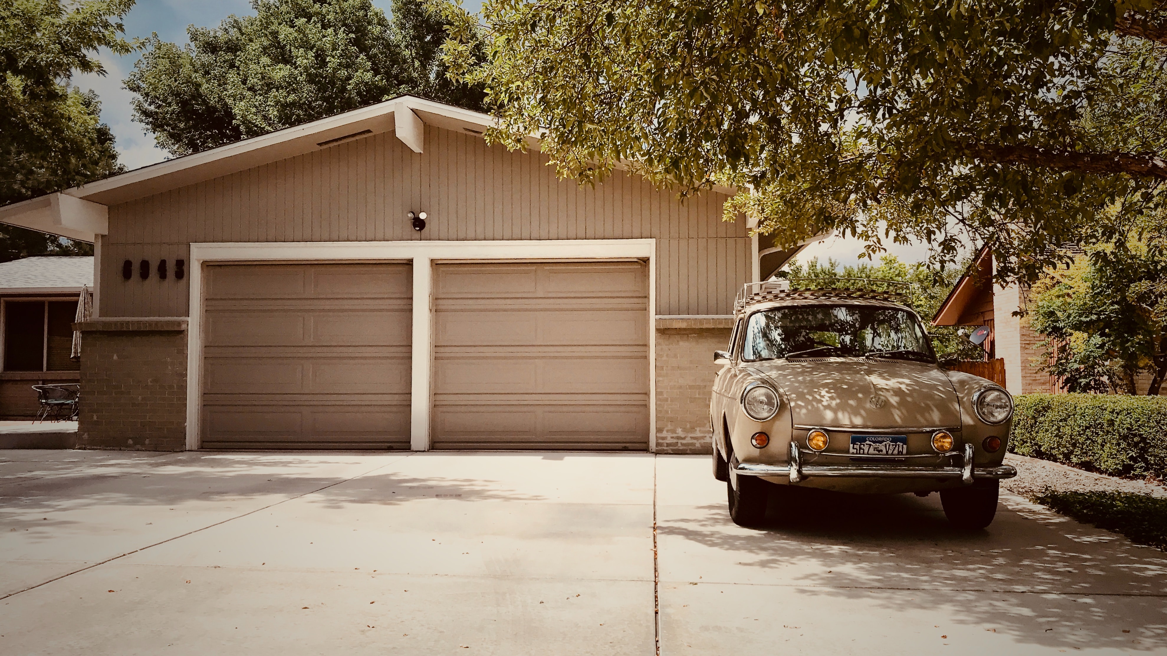 A beige house with a split double garage, with a car parked in the driveway.