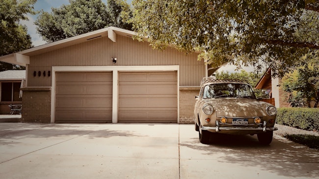 A beige house with a split double garage, with a car parked in the driveway.