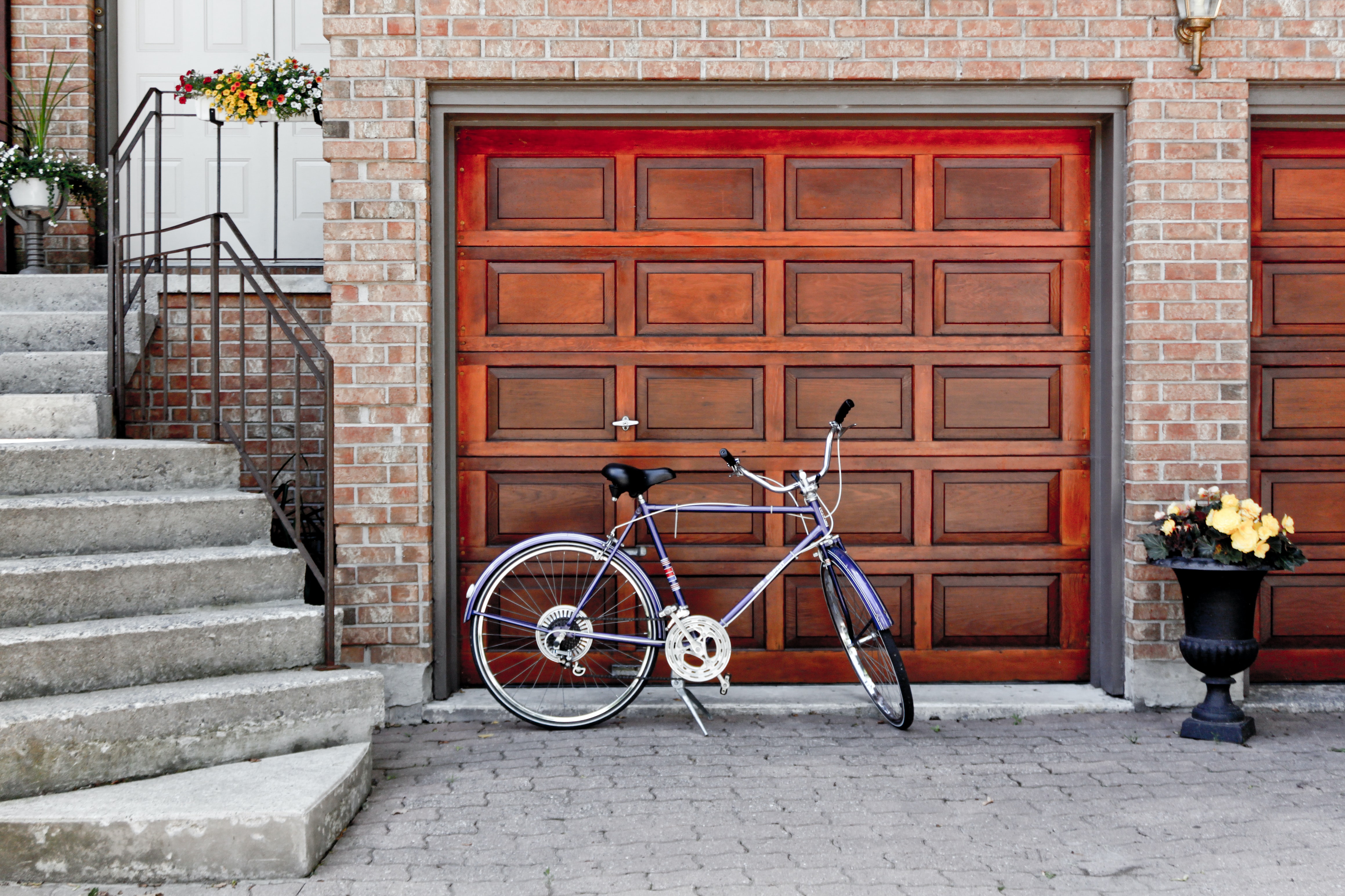 Purple bike parked in front of a red garage at the bottom of stairs leading to the front door of a house.