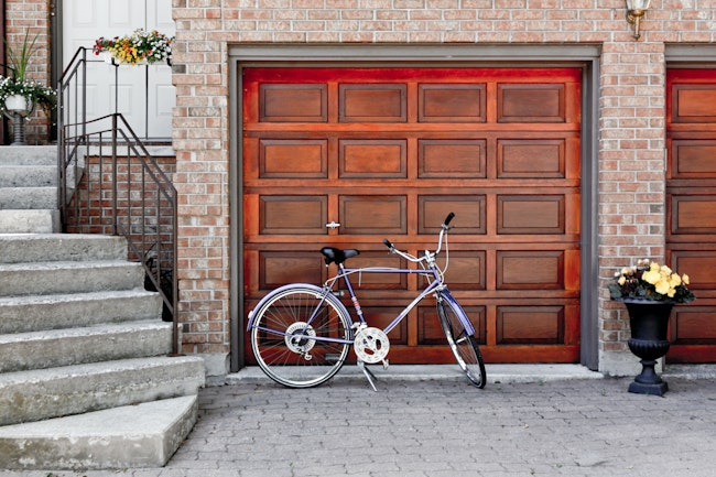 Purple bike parked in front of a red garage at the bottom of stairs leading to the front door of a house.