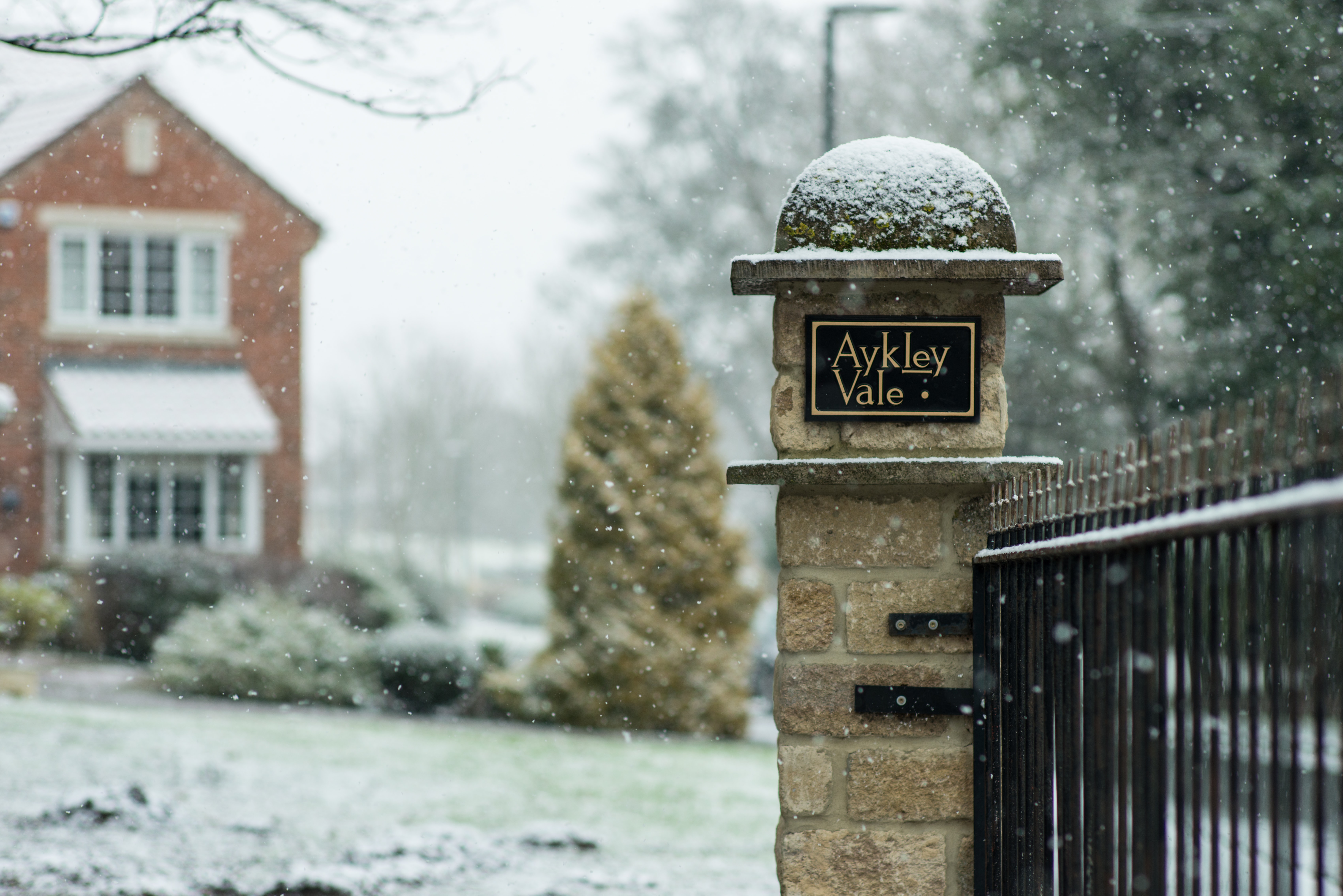 A red brick home behind a gate in the snow.