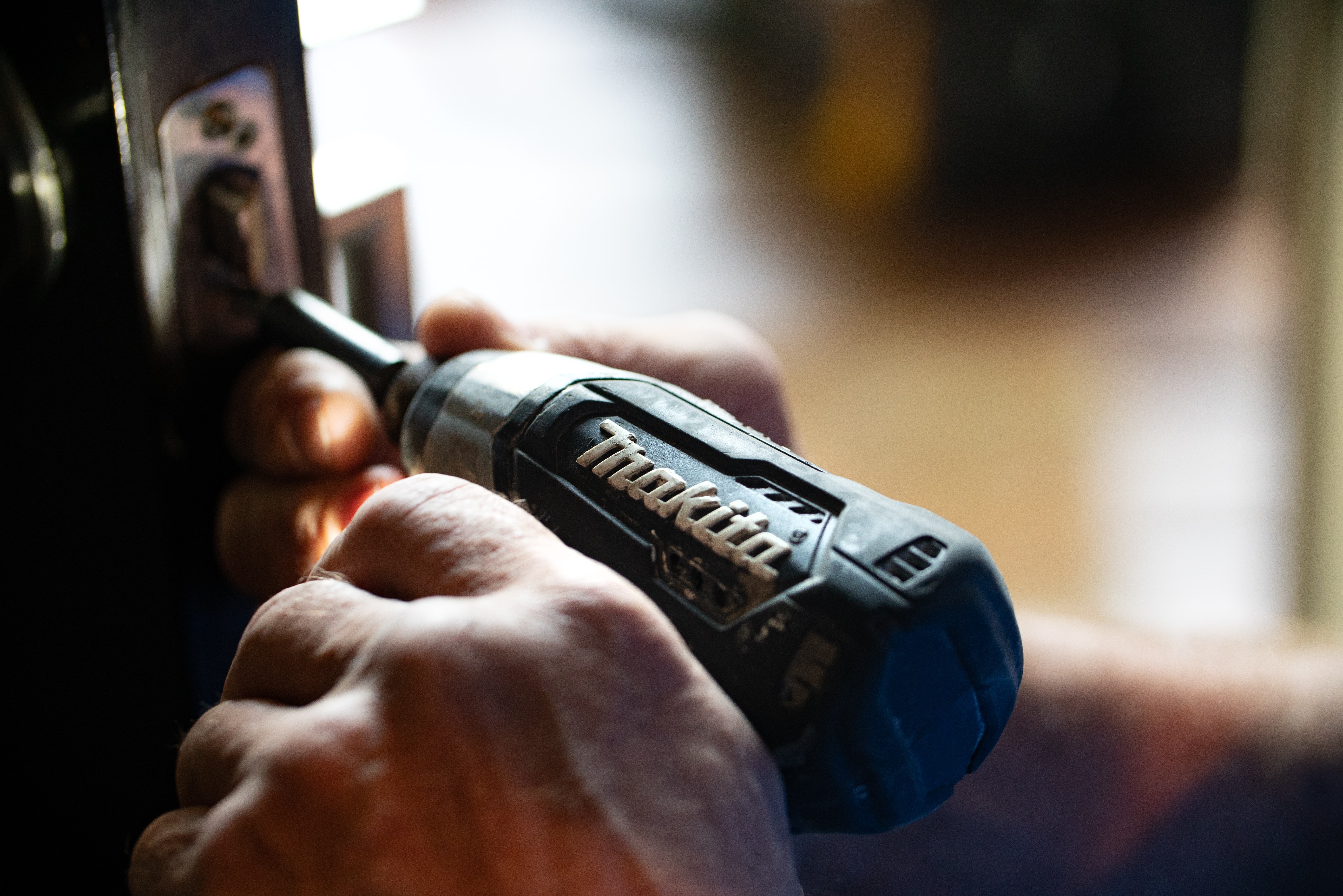 Homeowner fixing the lock on their front door with a drill.