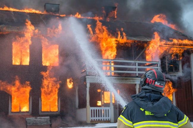 A fire fighter uses a water hose to battle a house fire.