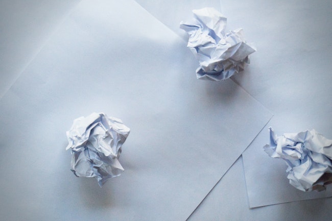 Three crumpled pieces of paper on top of regular paper on the ground.