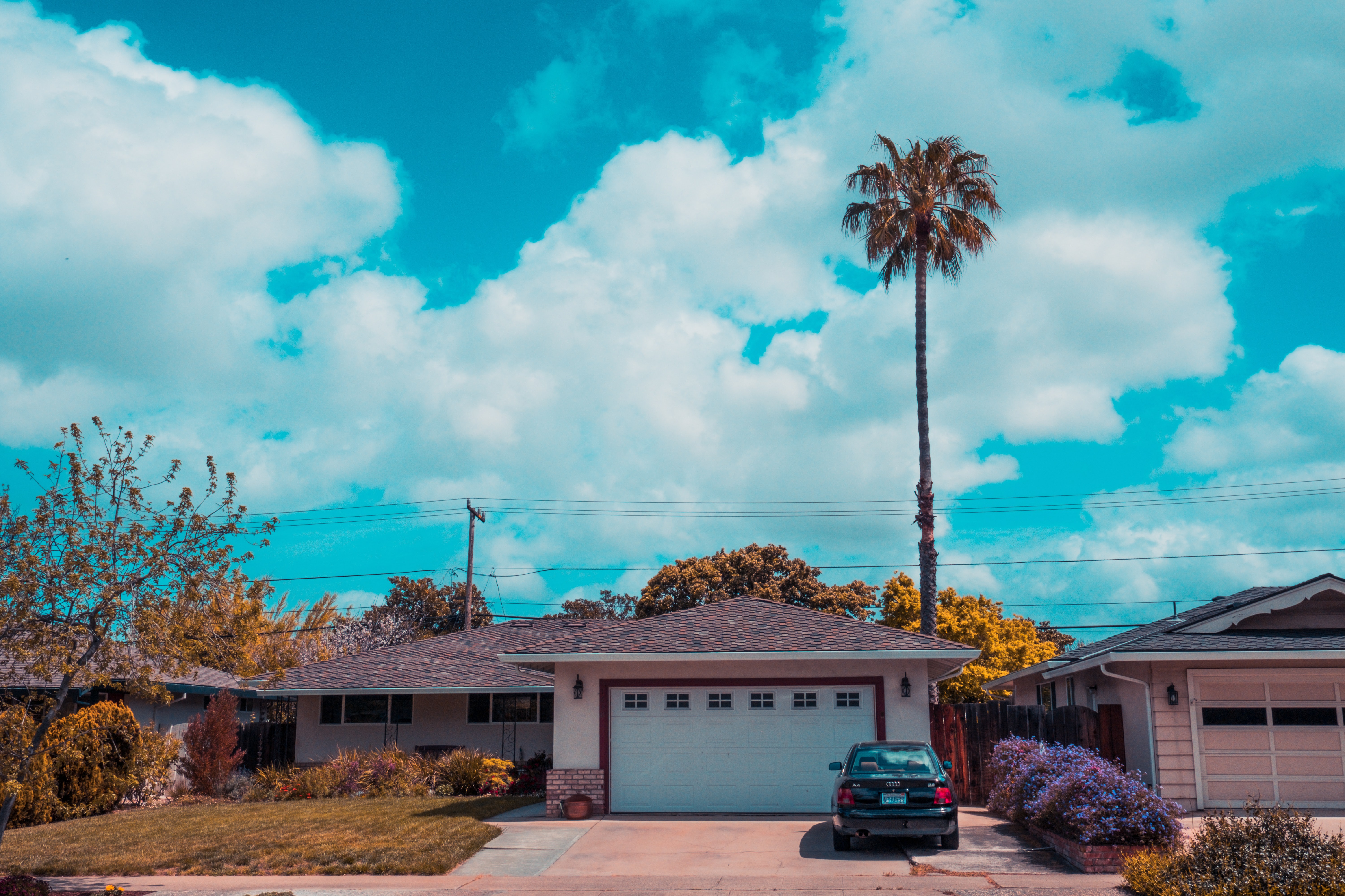 One level home with a garage and car and a palm tree.