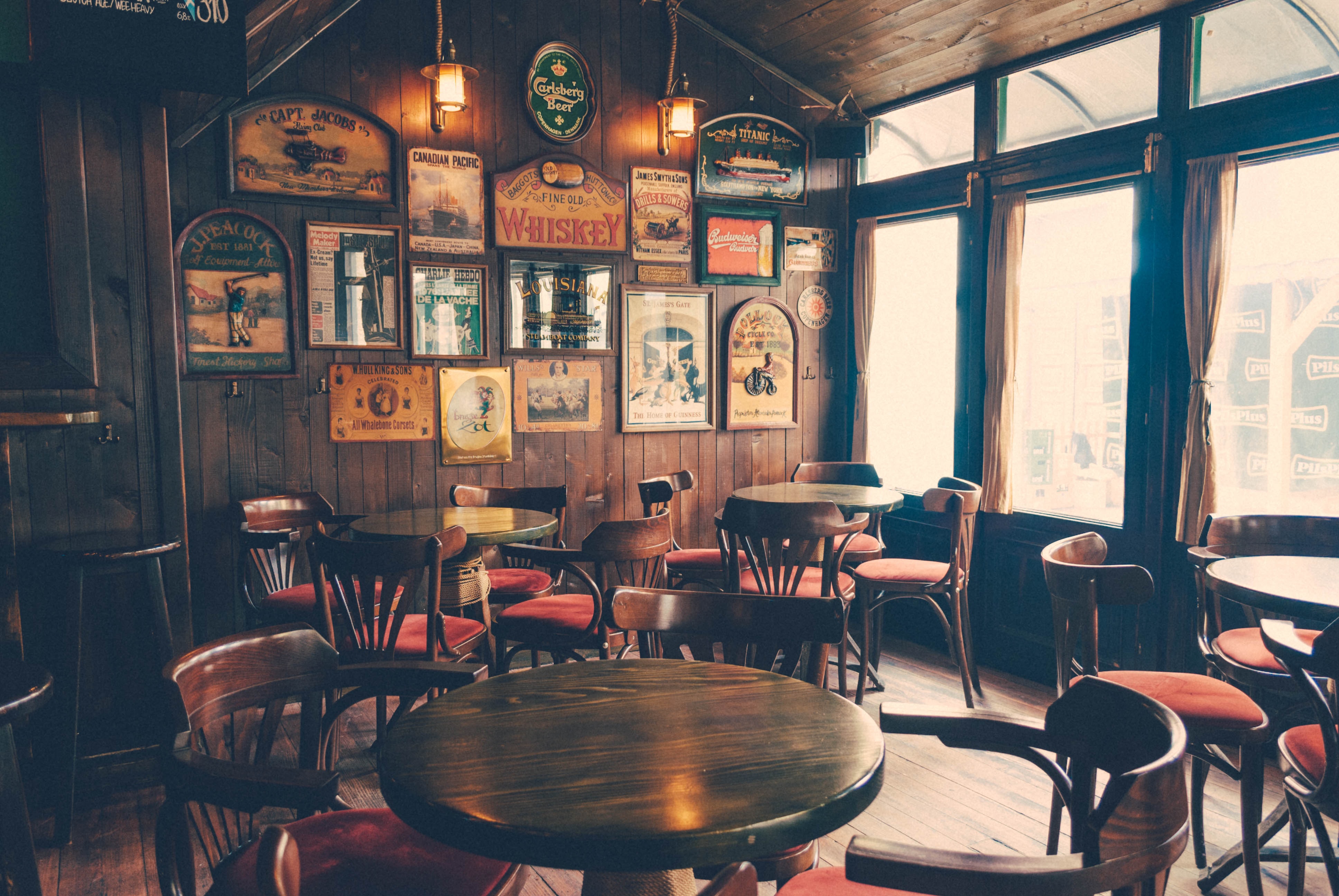 An empty pub with old signs on the wall and round wood tables.