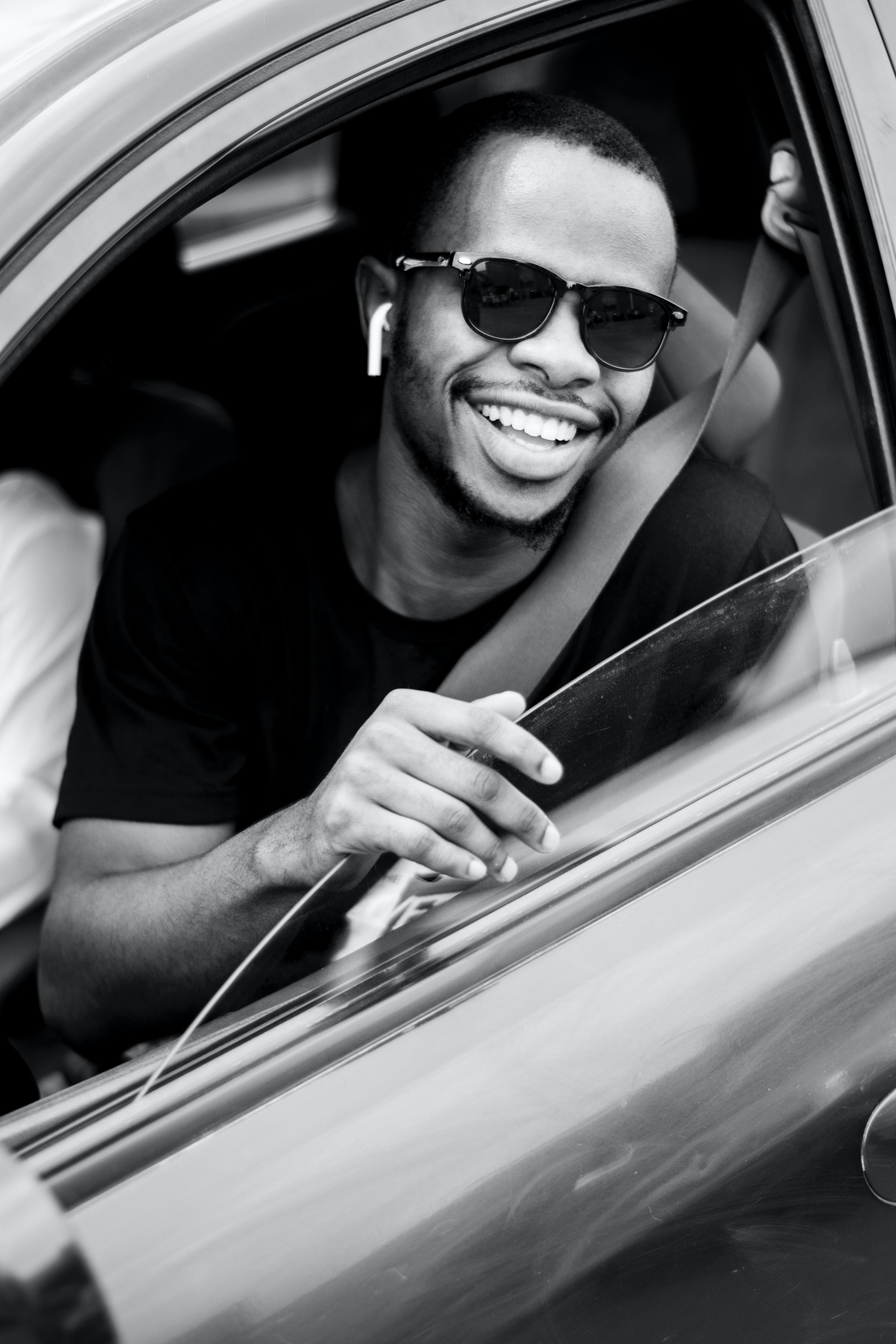 A rideshare driver in the front seat of a car smiling.