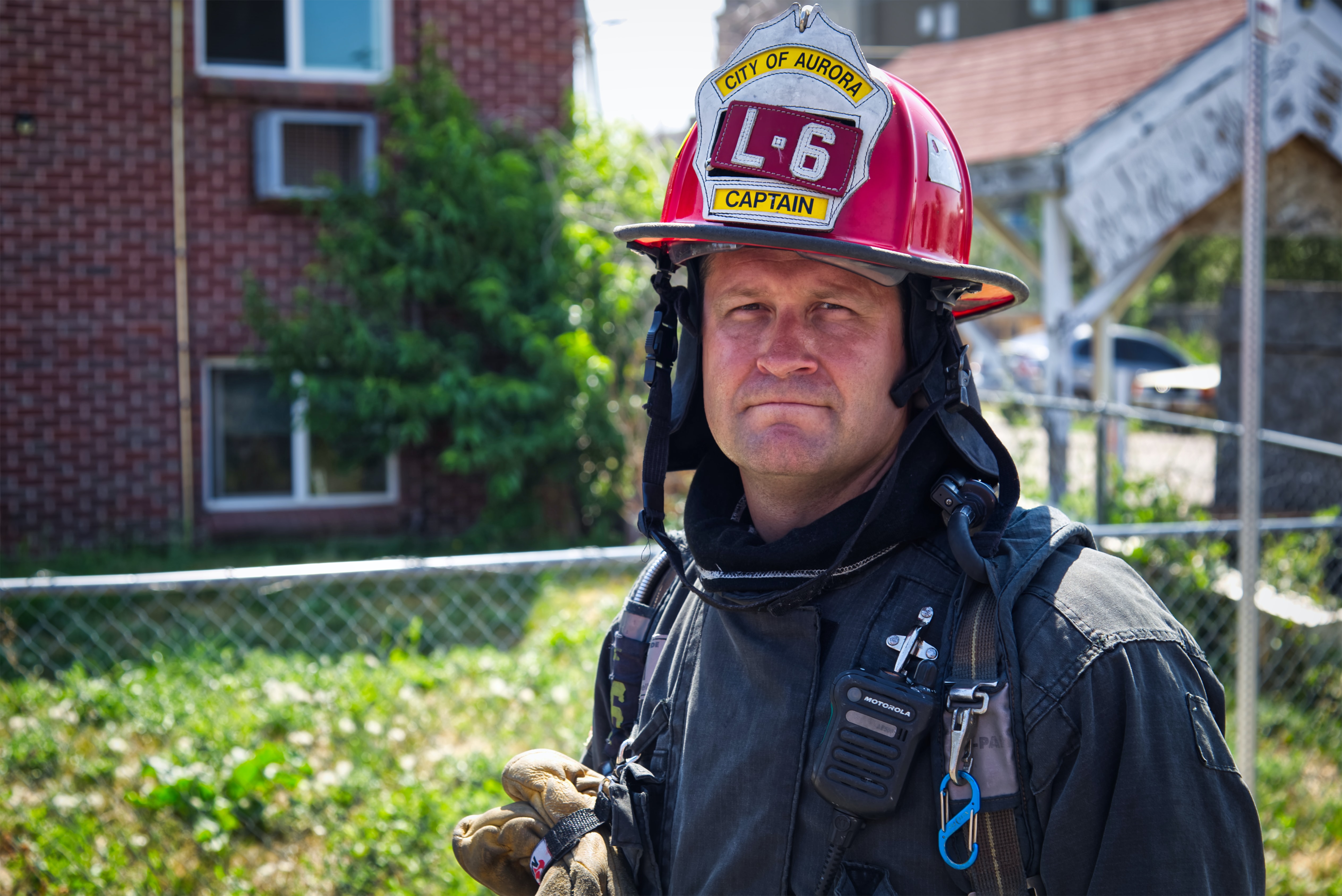 Fire captain with hat and coat on standing in front of a brick house.