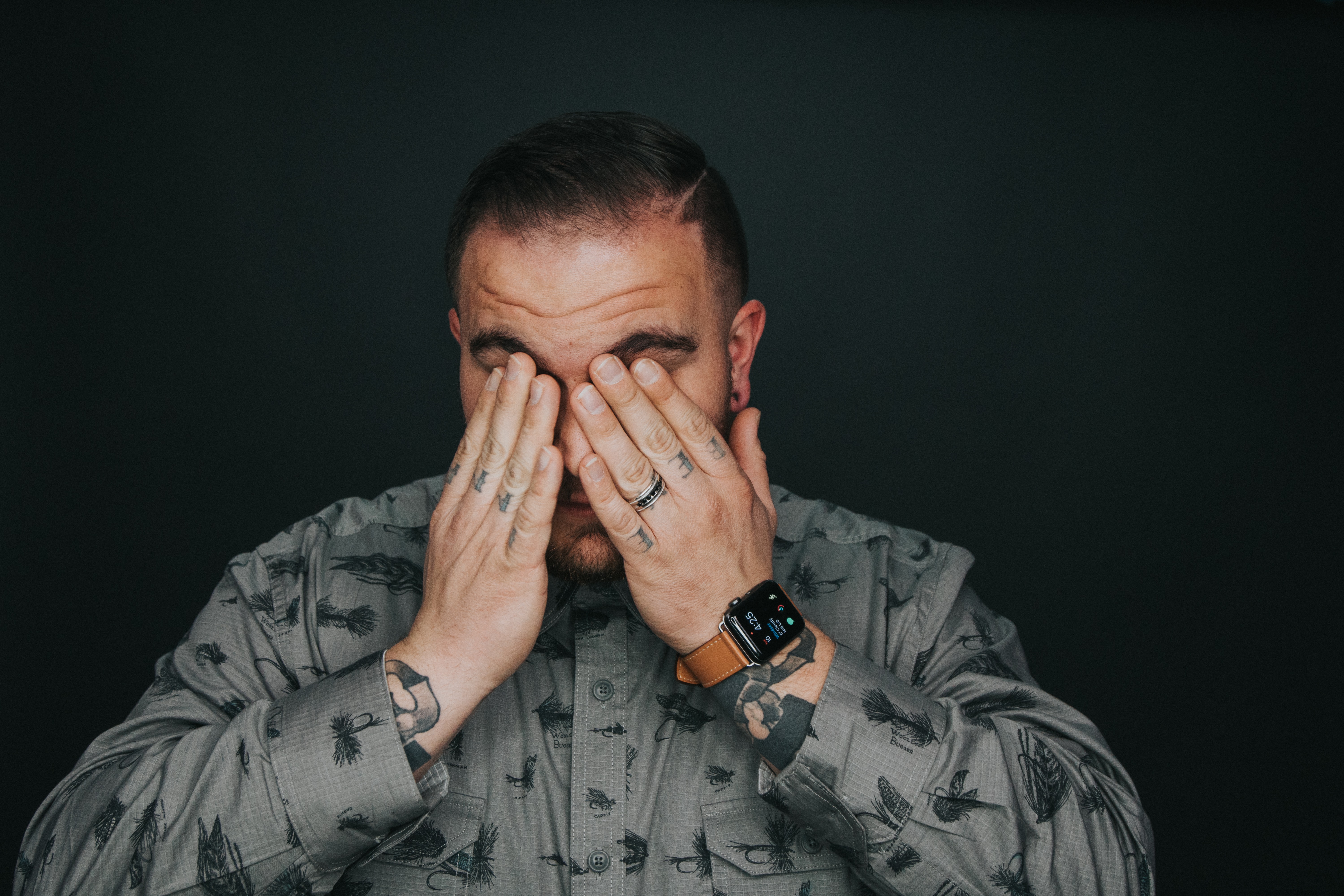 Man in a gray shirt with hands over his eyes as if in pain.