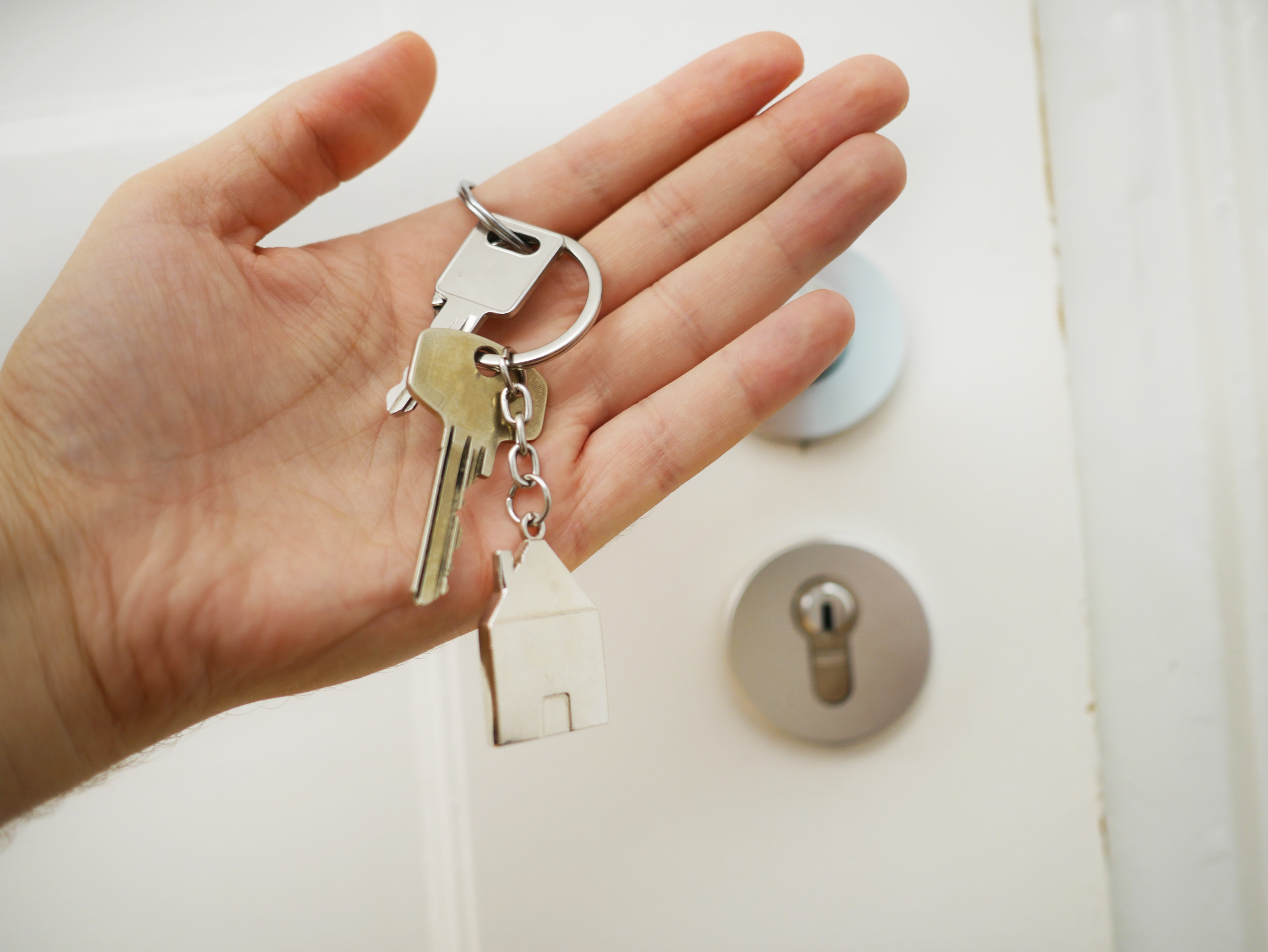 Person's hand holding a set of house keys in front of a door.
