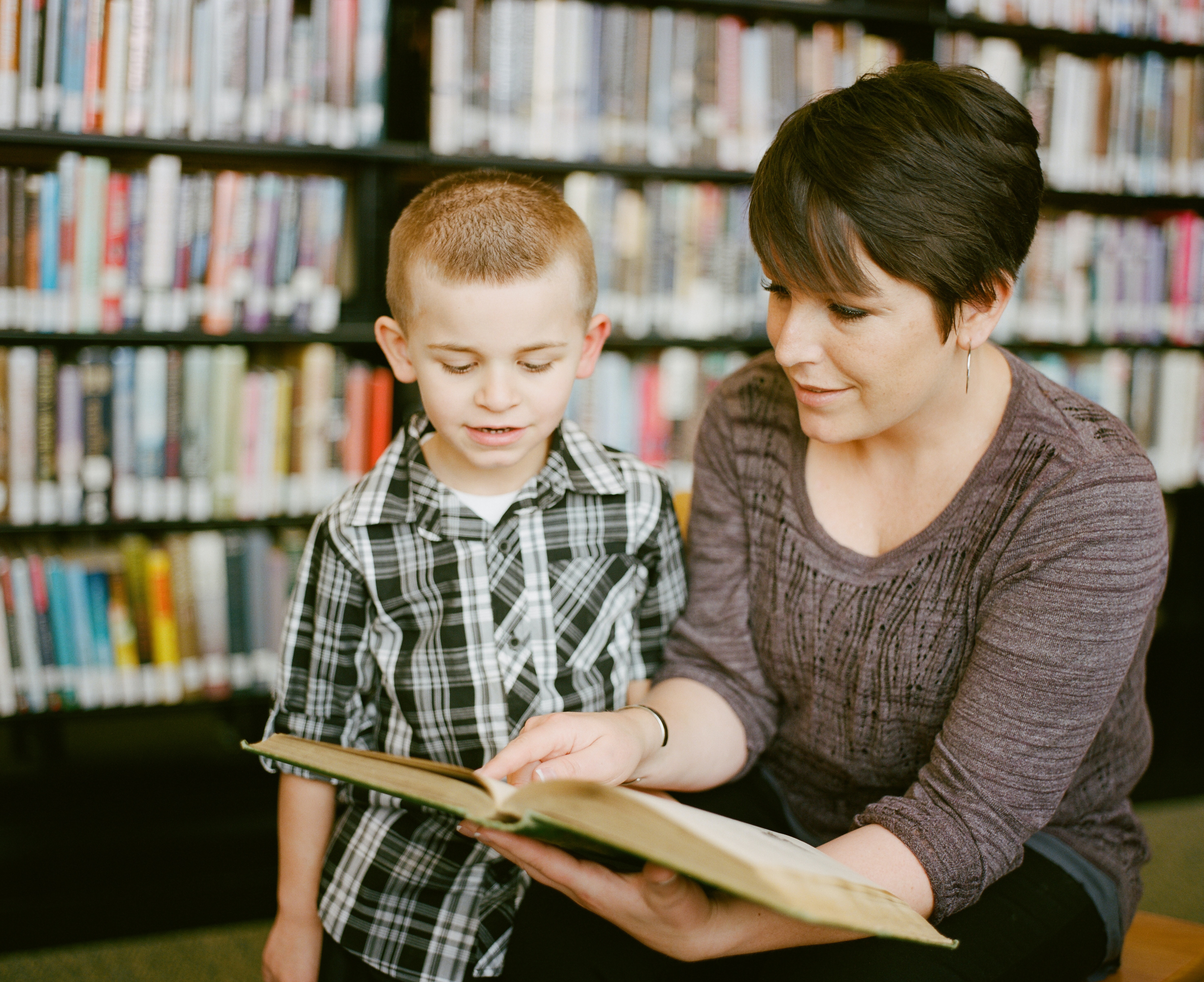 School teacher helping a young student read a book.