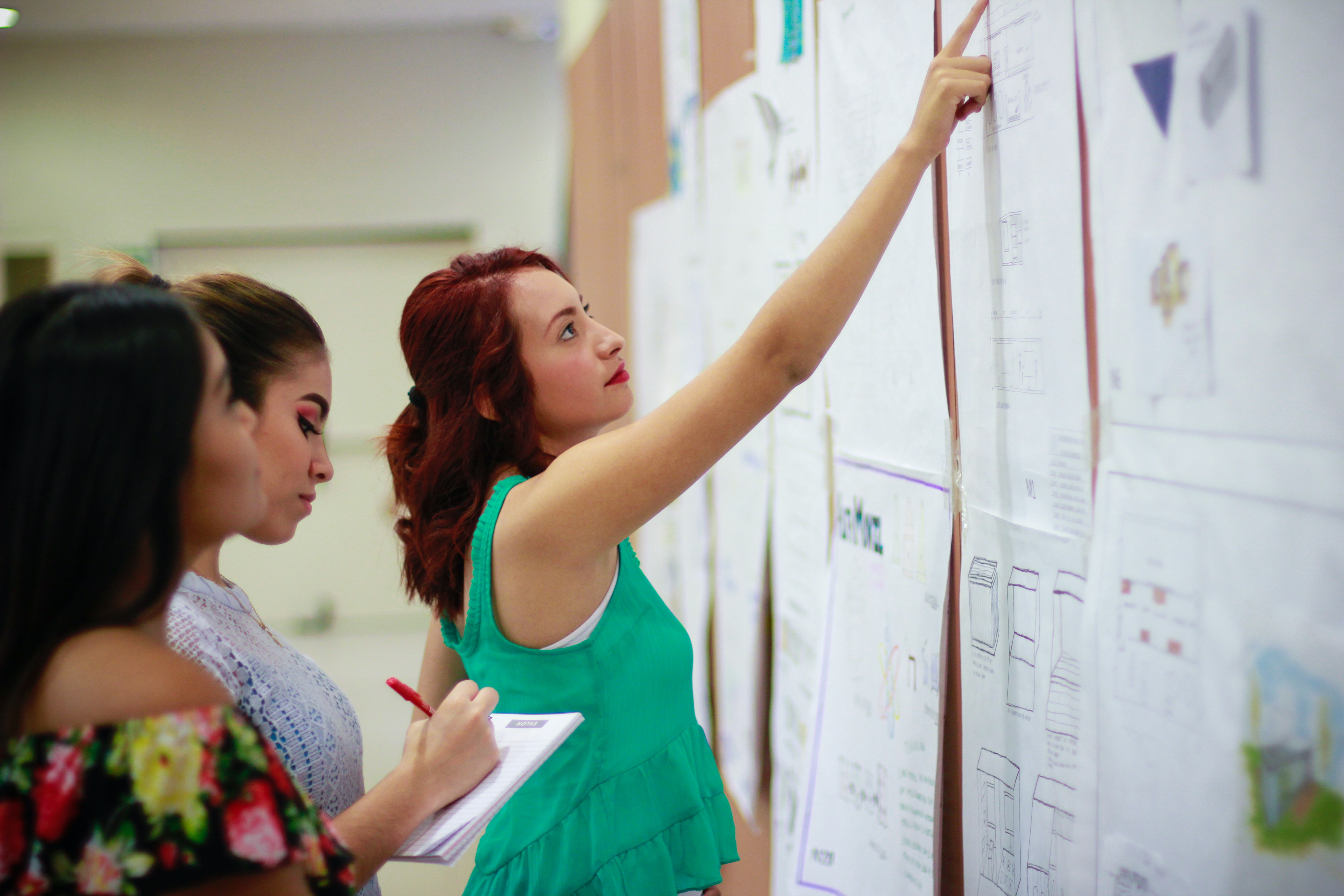 Teacher pointing to a paper on a bulletin board while others look.