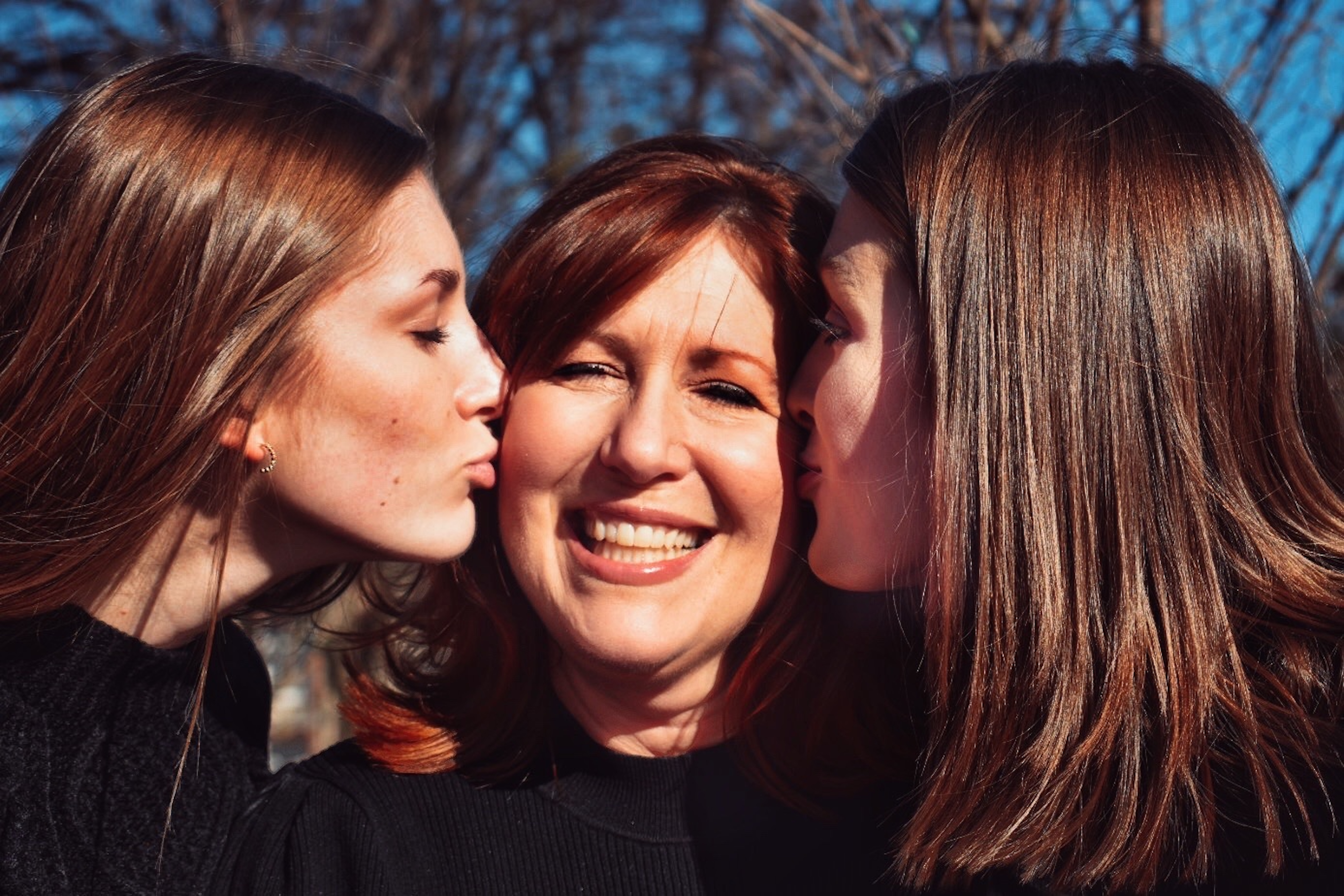 Two adult daughters kissing their mom on the cheek.