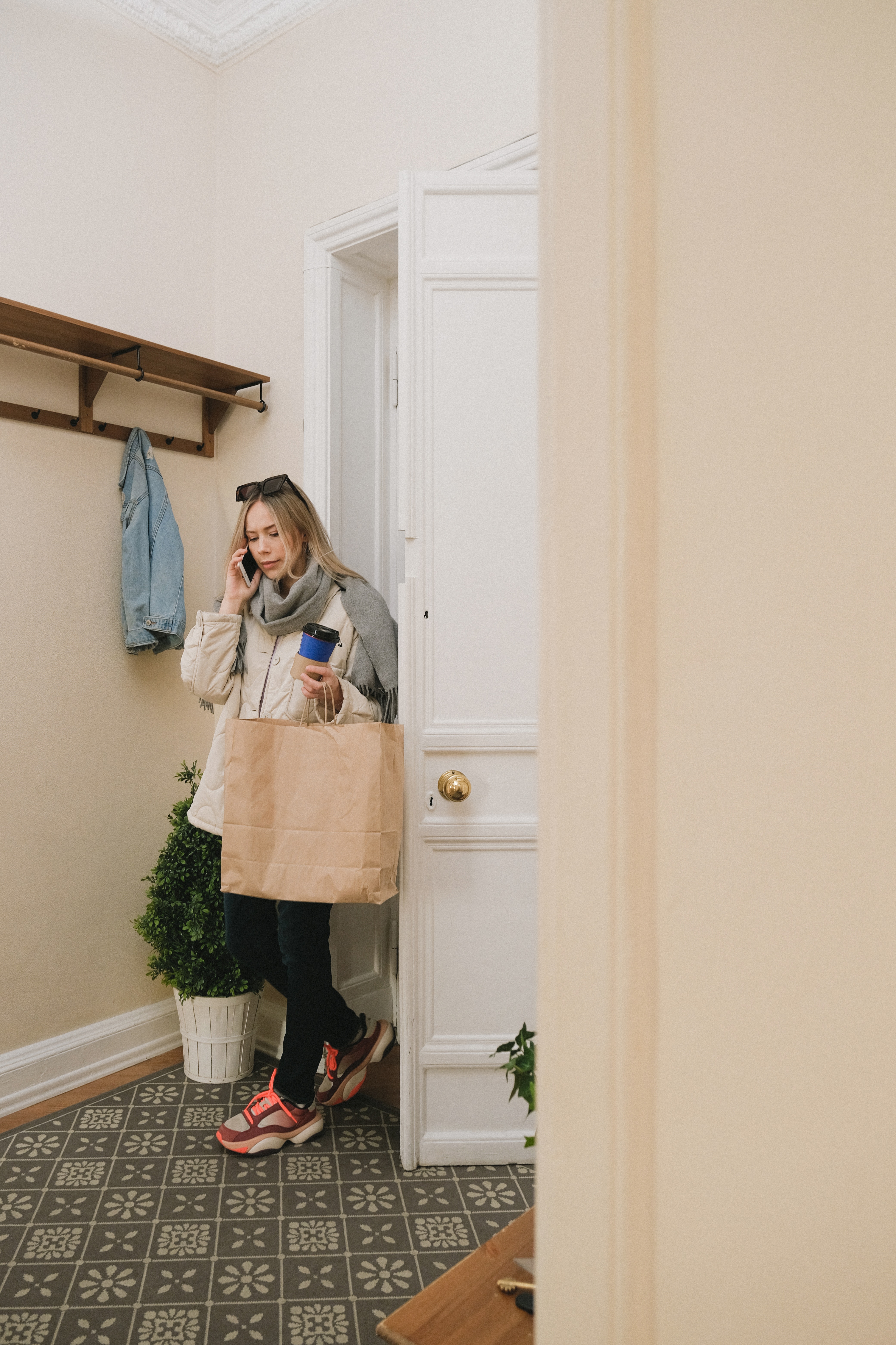 Woman coming into her home or apartment while talking on the phone and carrying a bag.