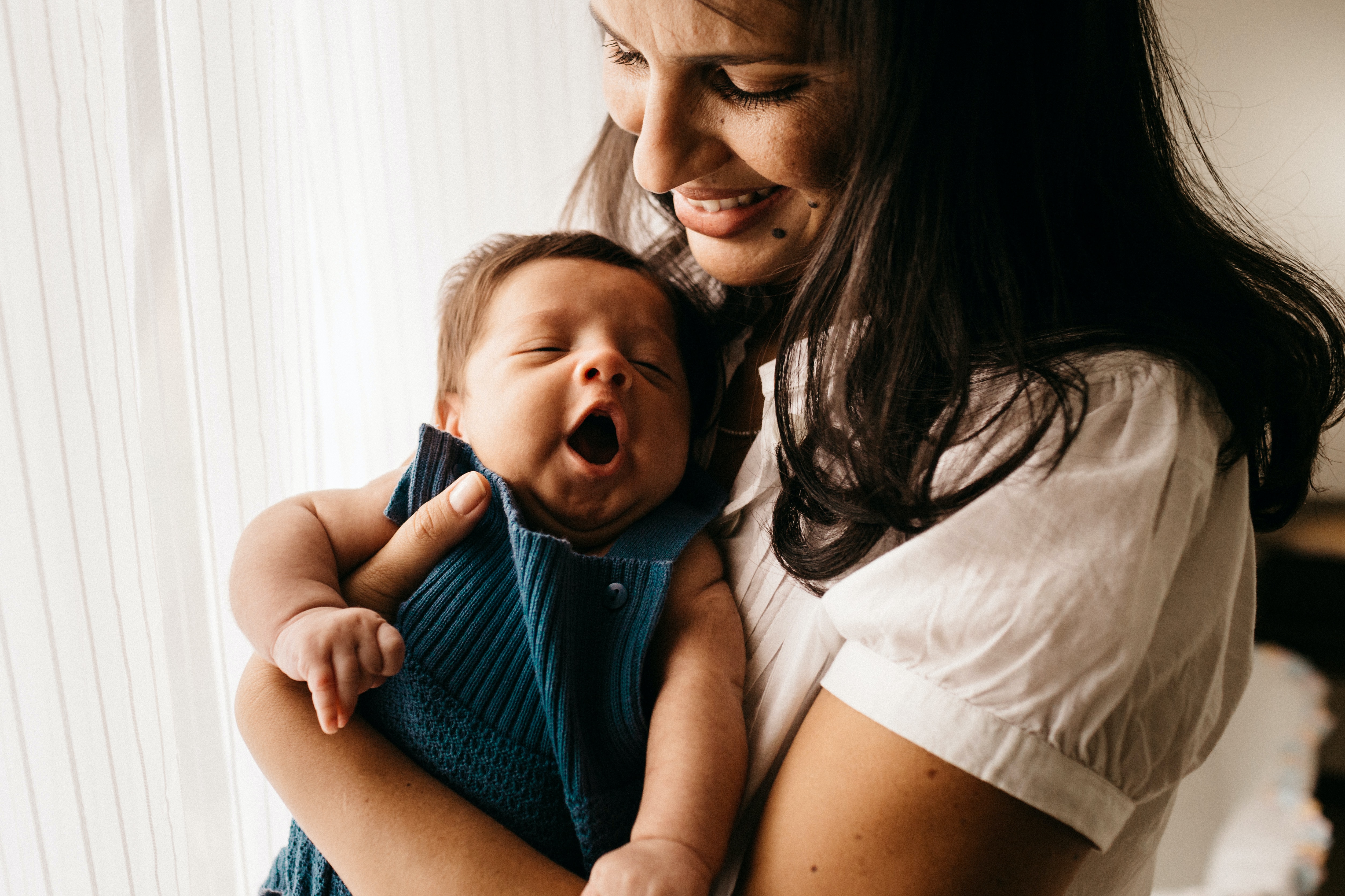 Mom holding a tiny baby at home by a window.