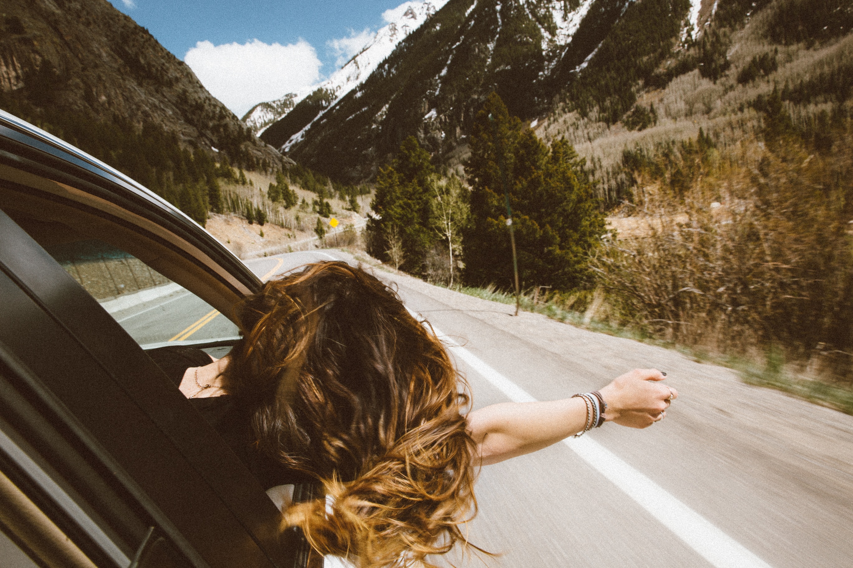 Woman enjoying the breeze out the window of her car on a road trip.