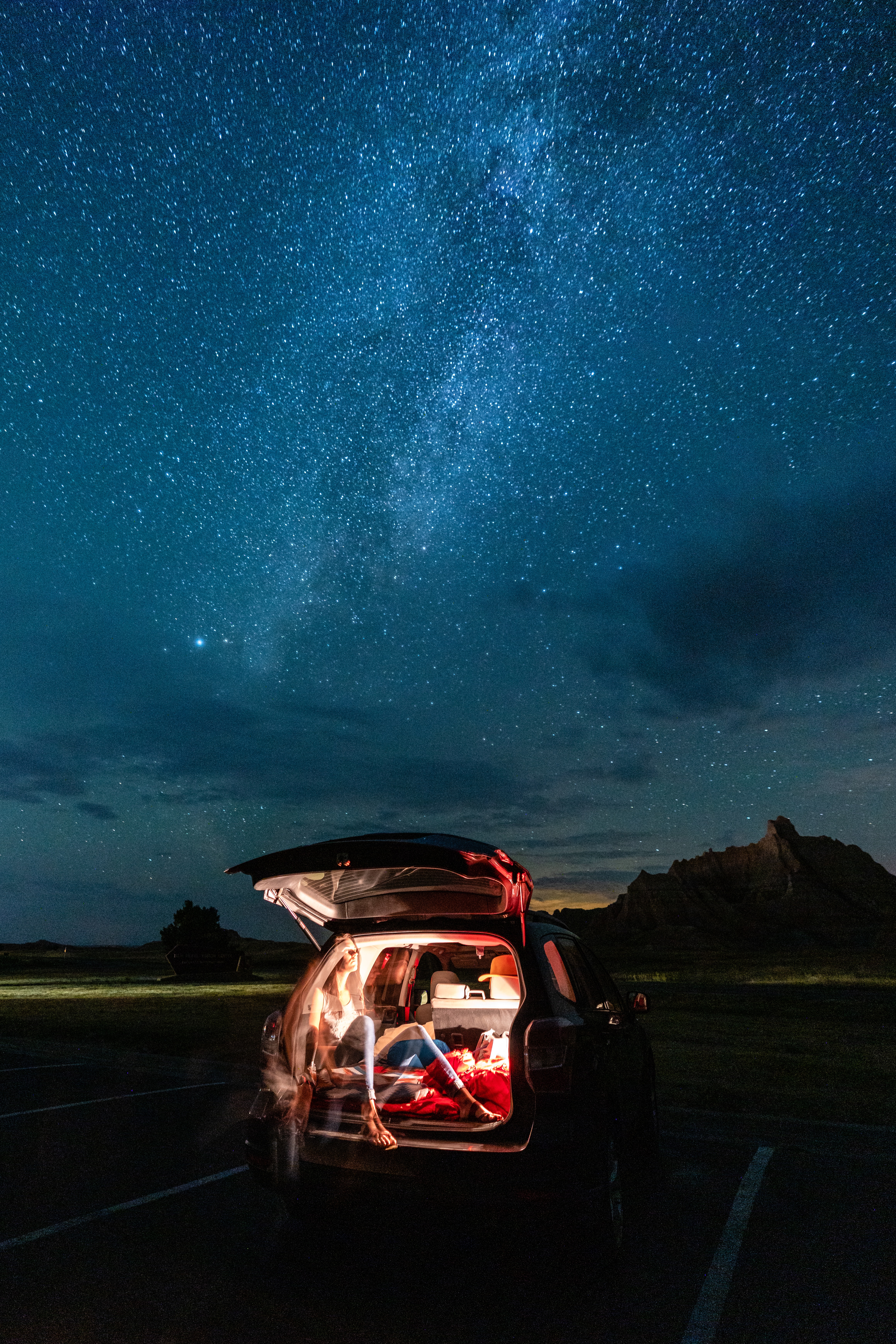 Person in the back of their car resting and looking out into the night sky filled with stars.