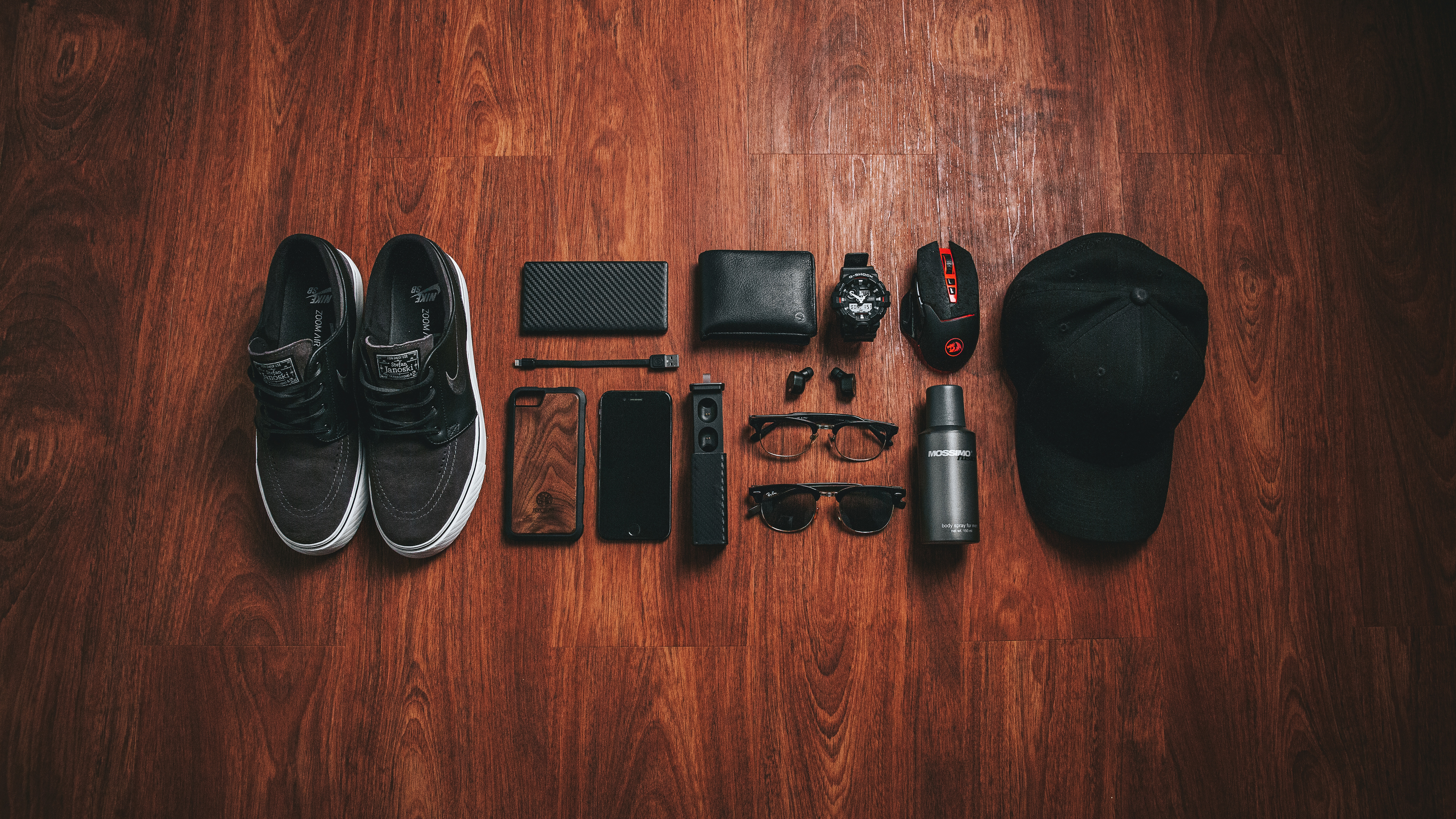 Packing essentials laid out neatly on the floor, including shoes, phone, wallet, sunglasses, watch, hat, etc.