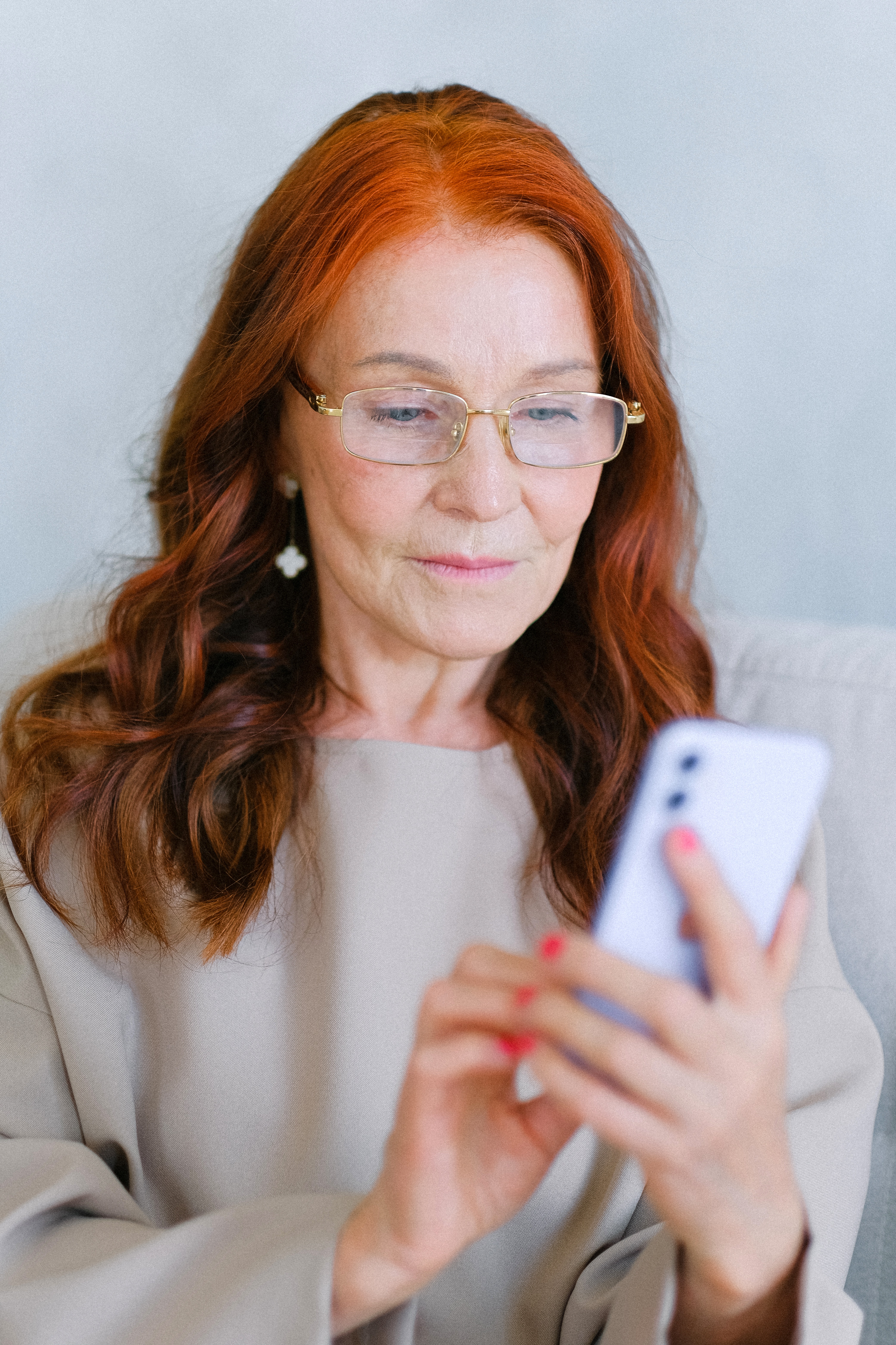 Older woman with red hair checking alerts on her cell phone.