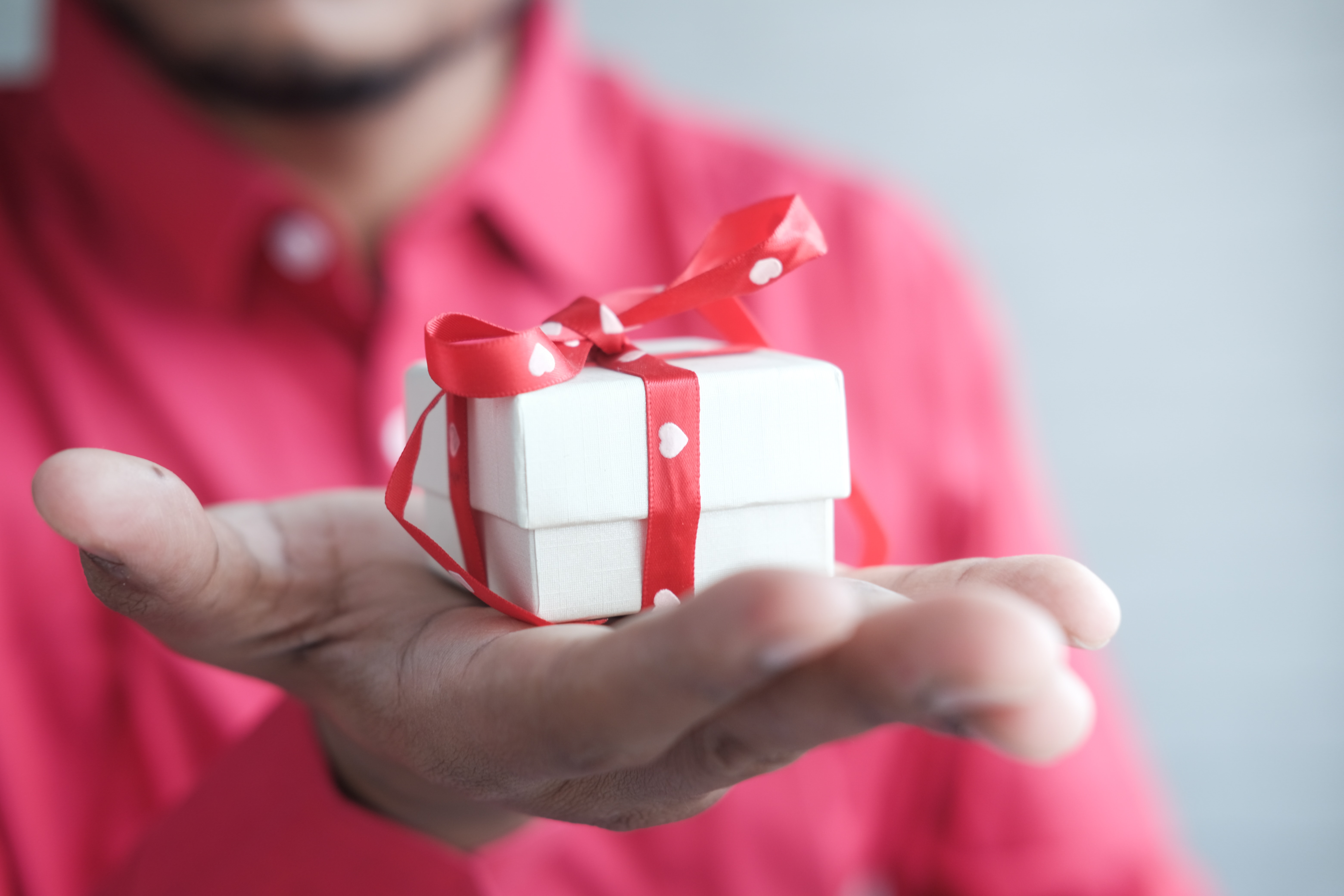 Man in a red shirt holding out his hand with a small white box gift in his hand.