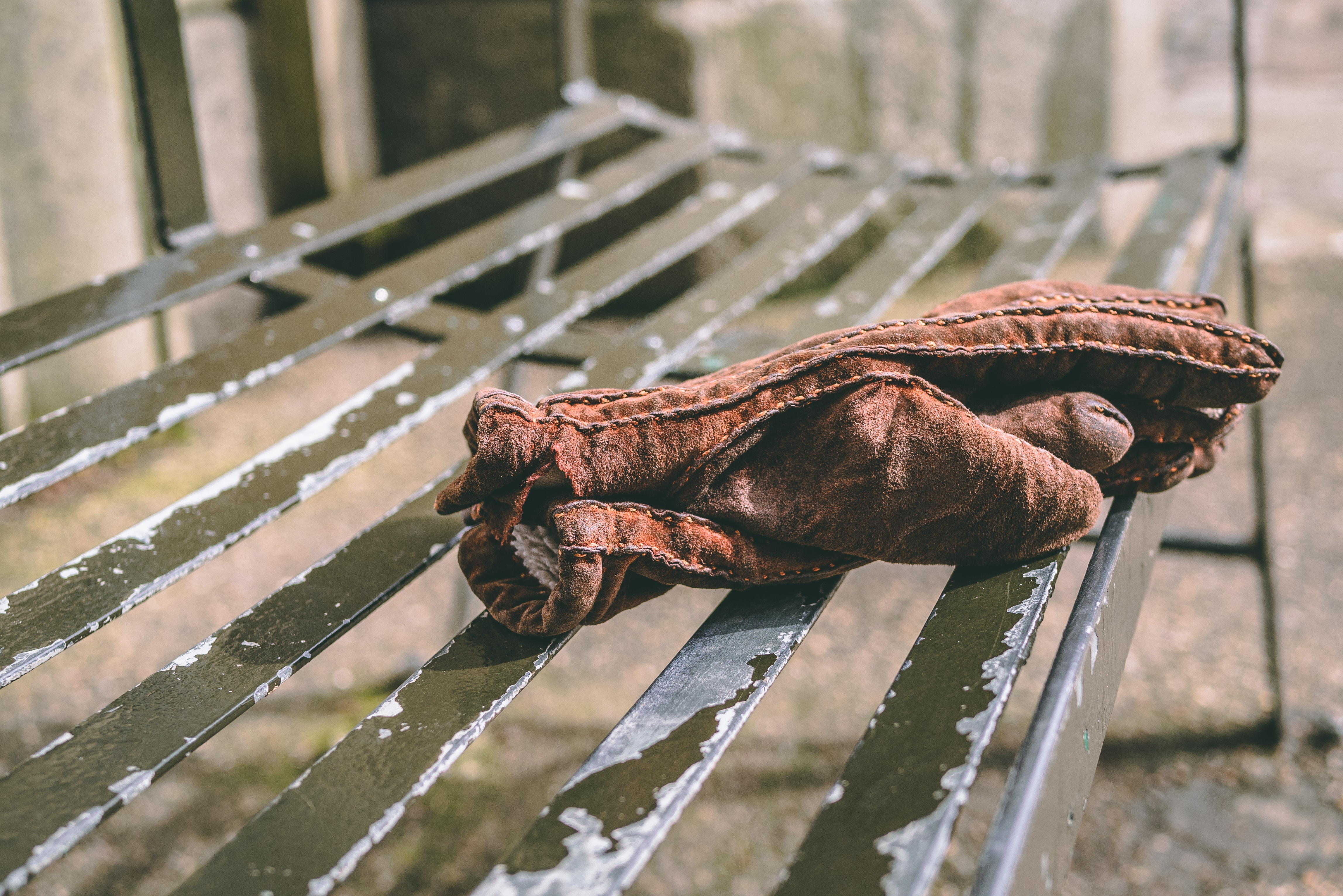 Old leather work gloves sitting on a metal bench.