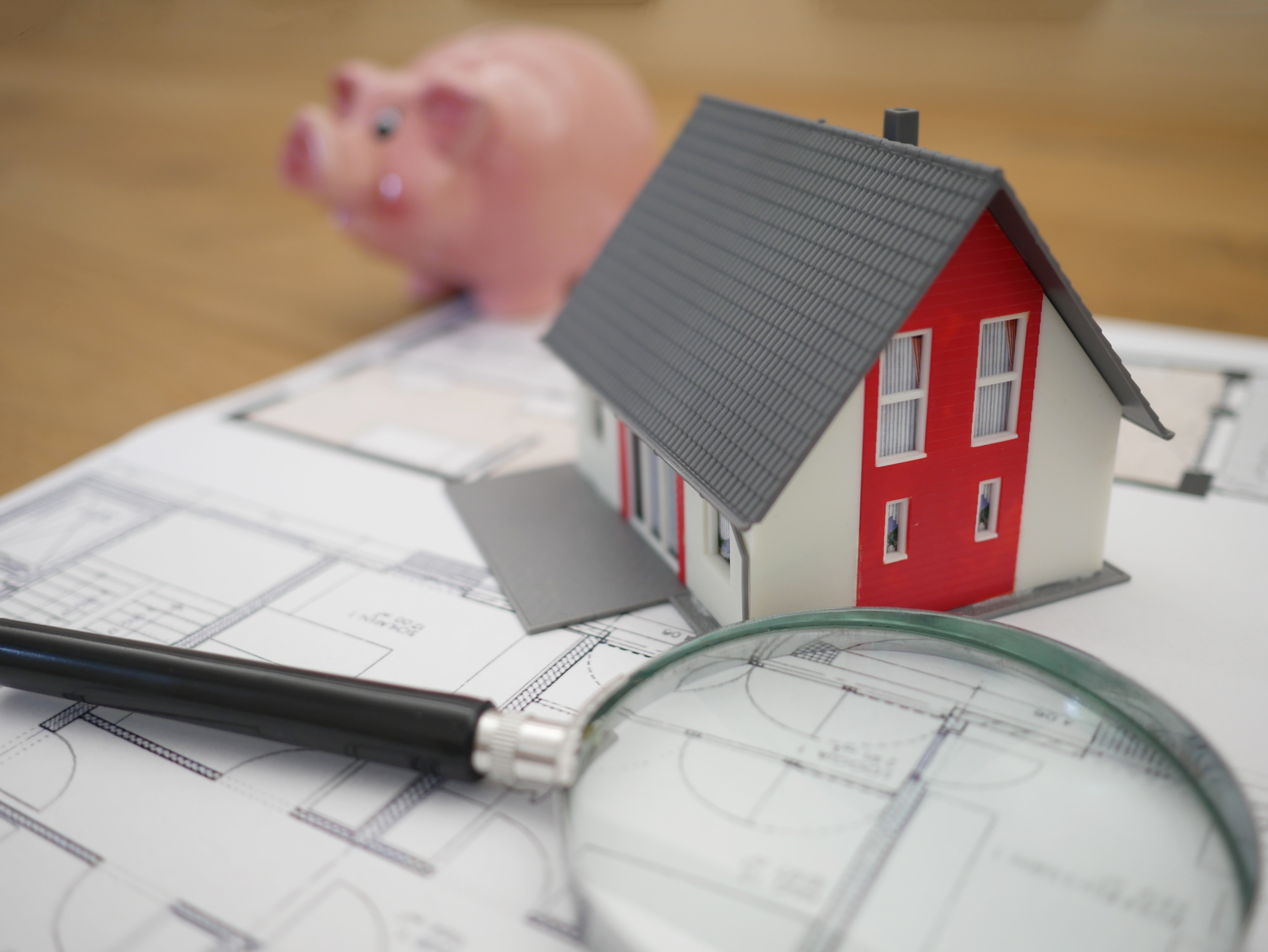 Mini house on a table with magnifying glass, house plans, and piggy bank.