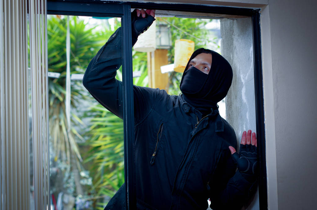 Burglar tampering with window to break into a house.