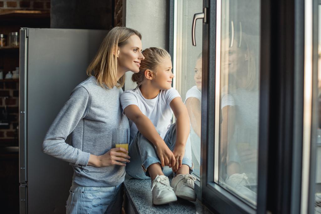 Mother and daughter in their home smiling as they look out the window.
