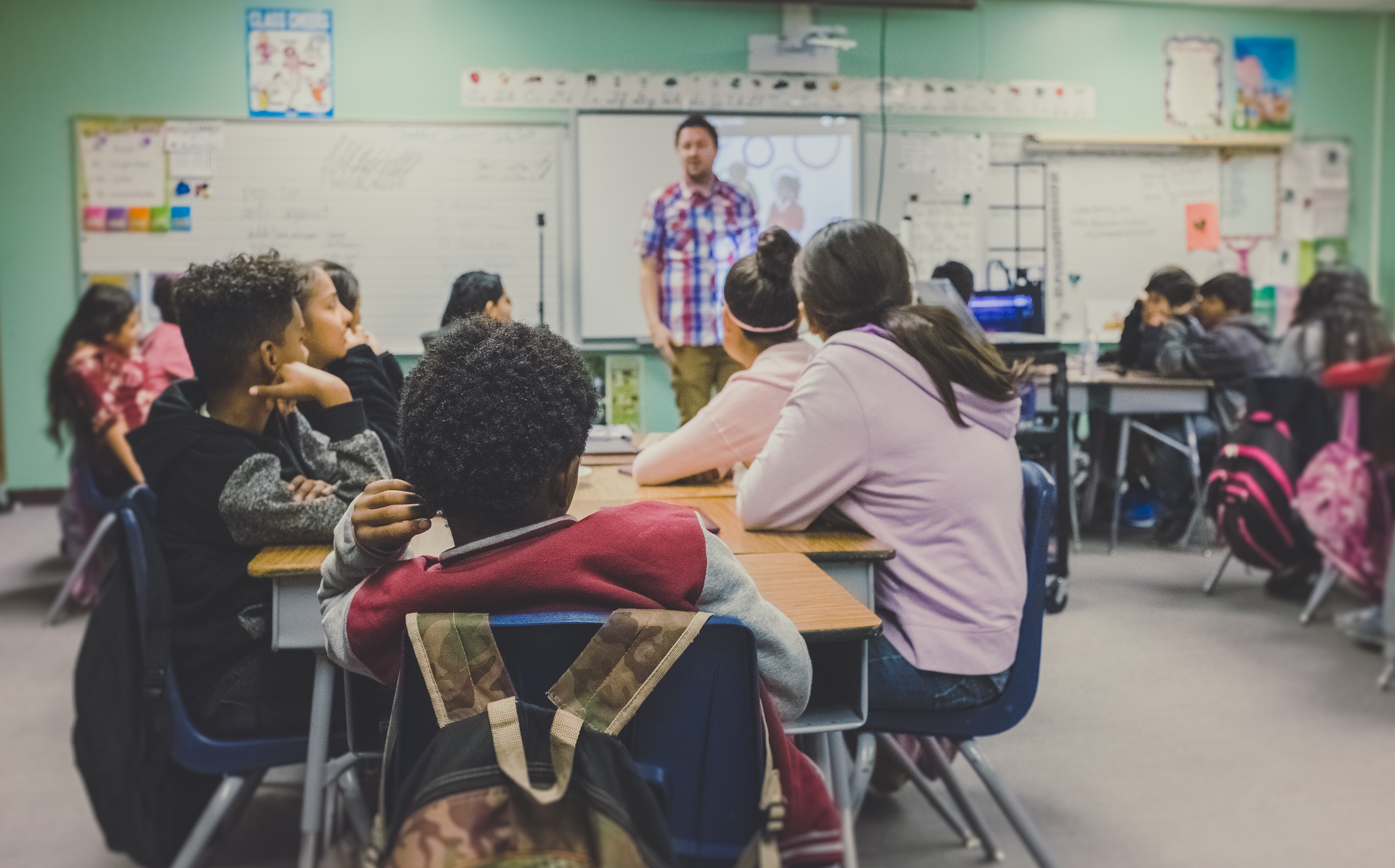 School teacher communicating with students sitting at desks.