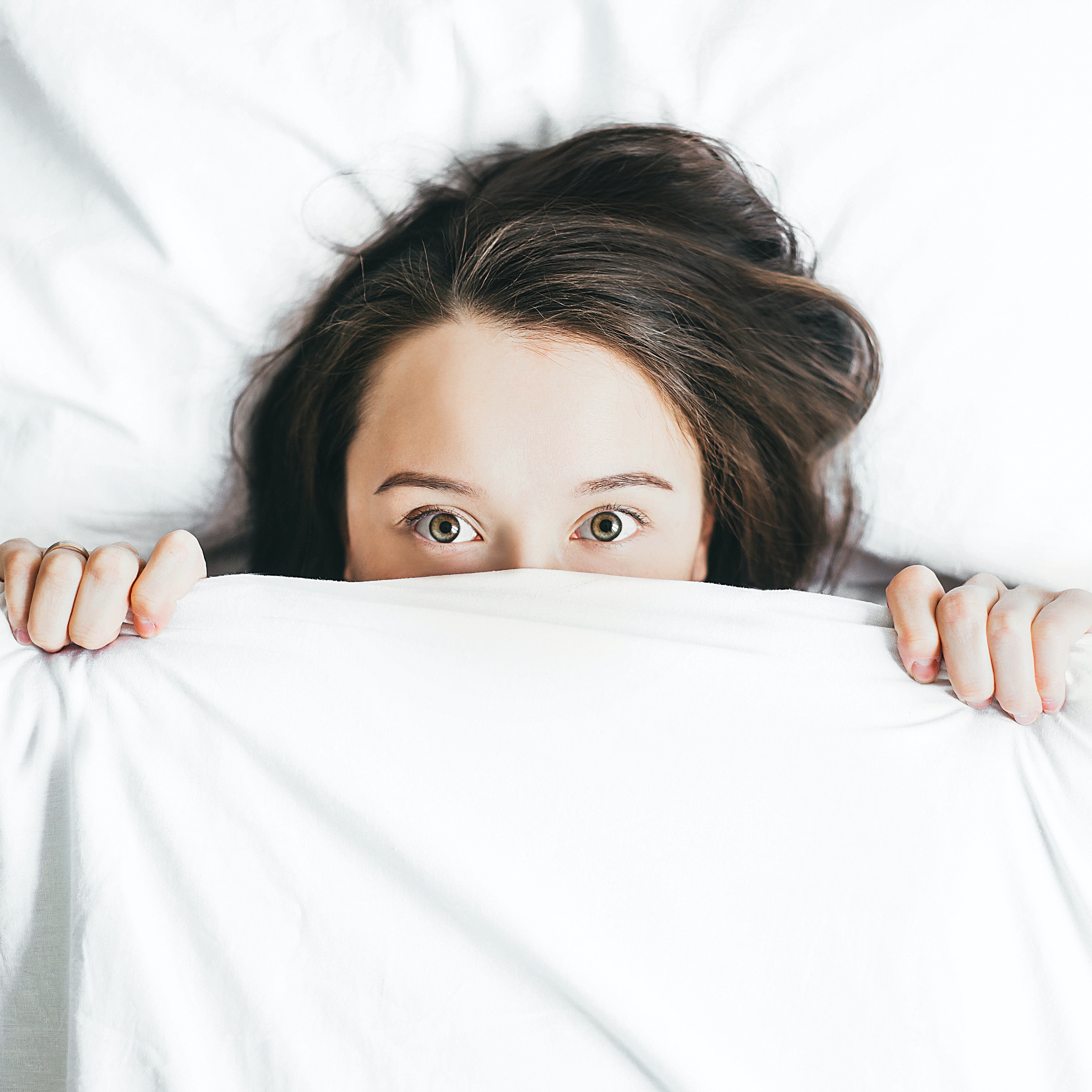 Woman awake in bed with blanket pulled up by her face.