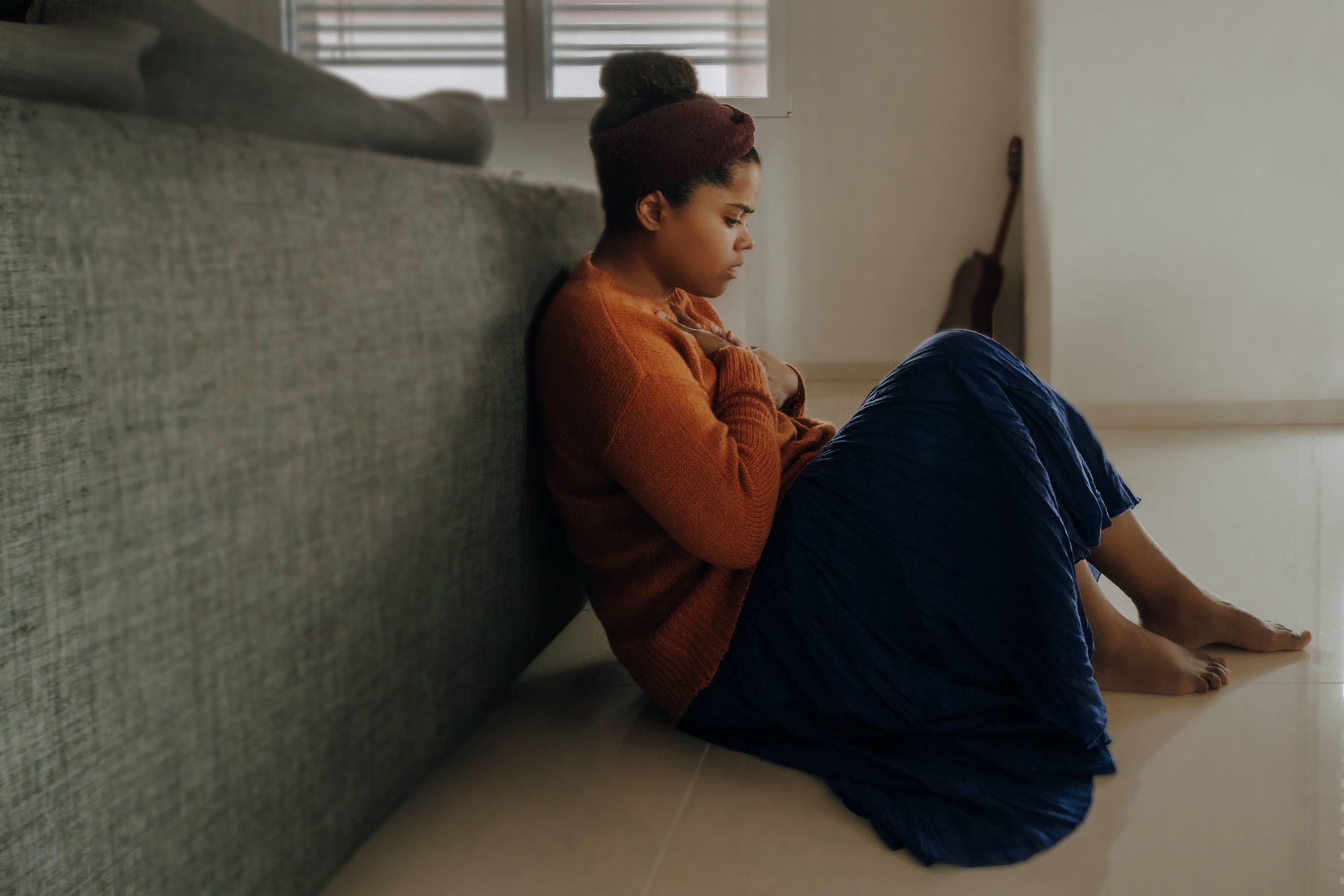 Anxious woman sitting on the floor next to her bed.