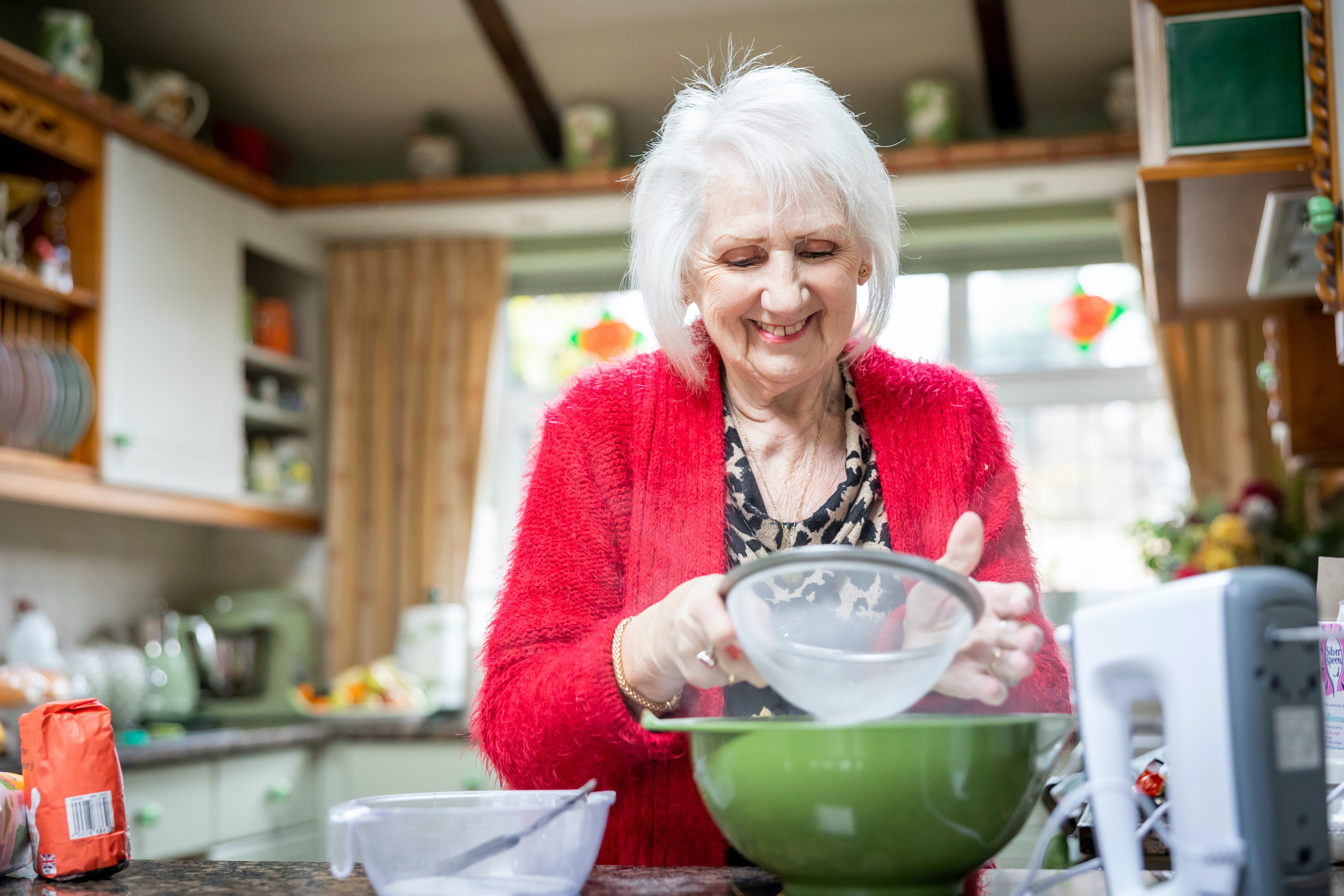 Elderly woman sifting flour in her kitchen at home.