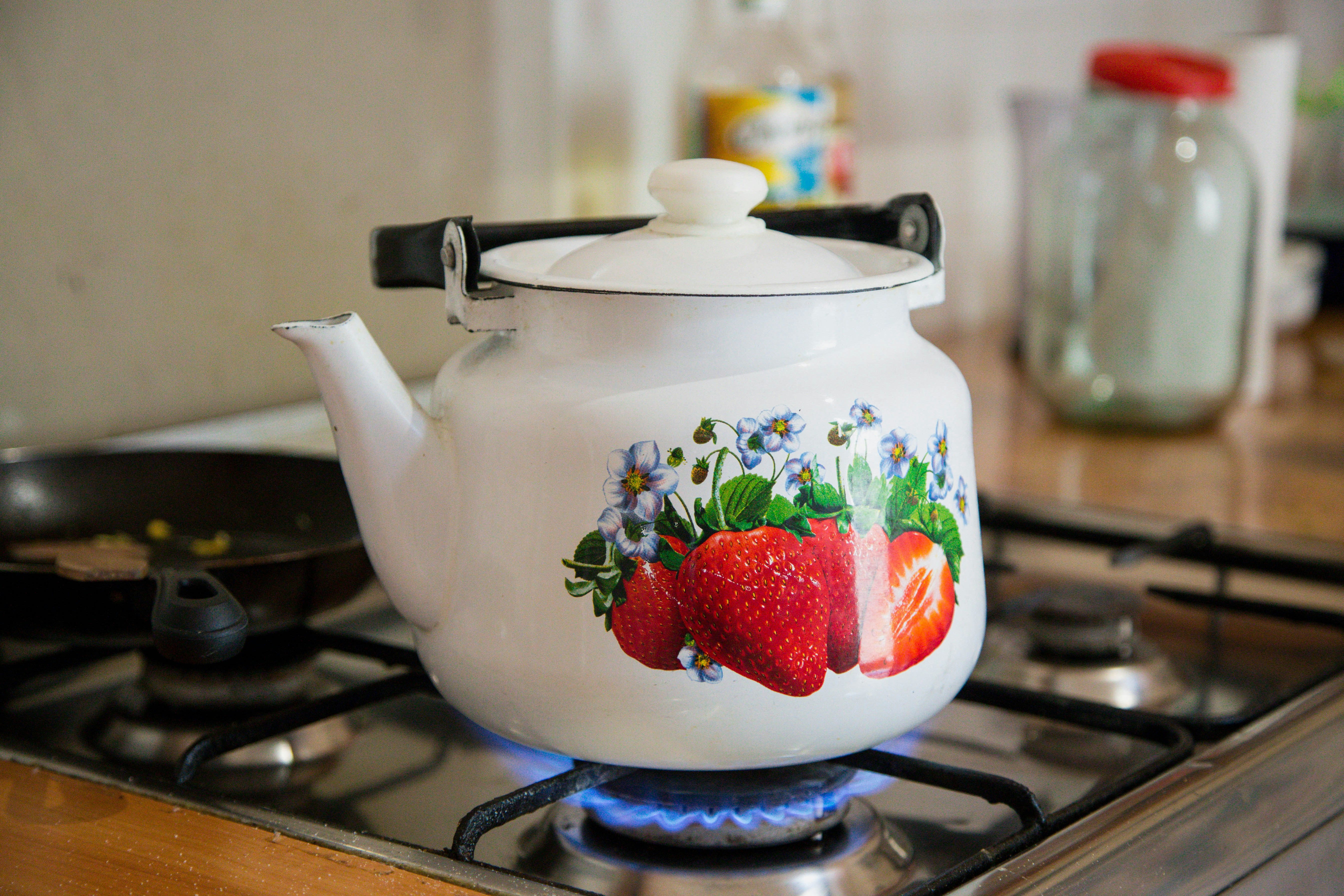 Tea pot with strawberries on it warming up over a gas stove.