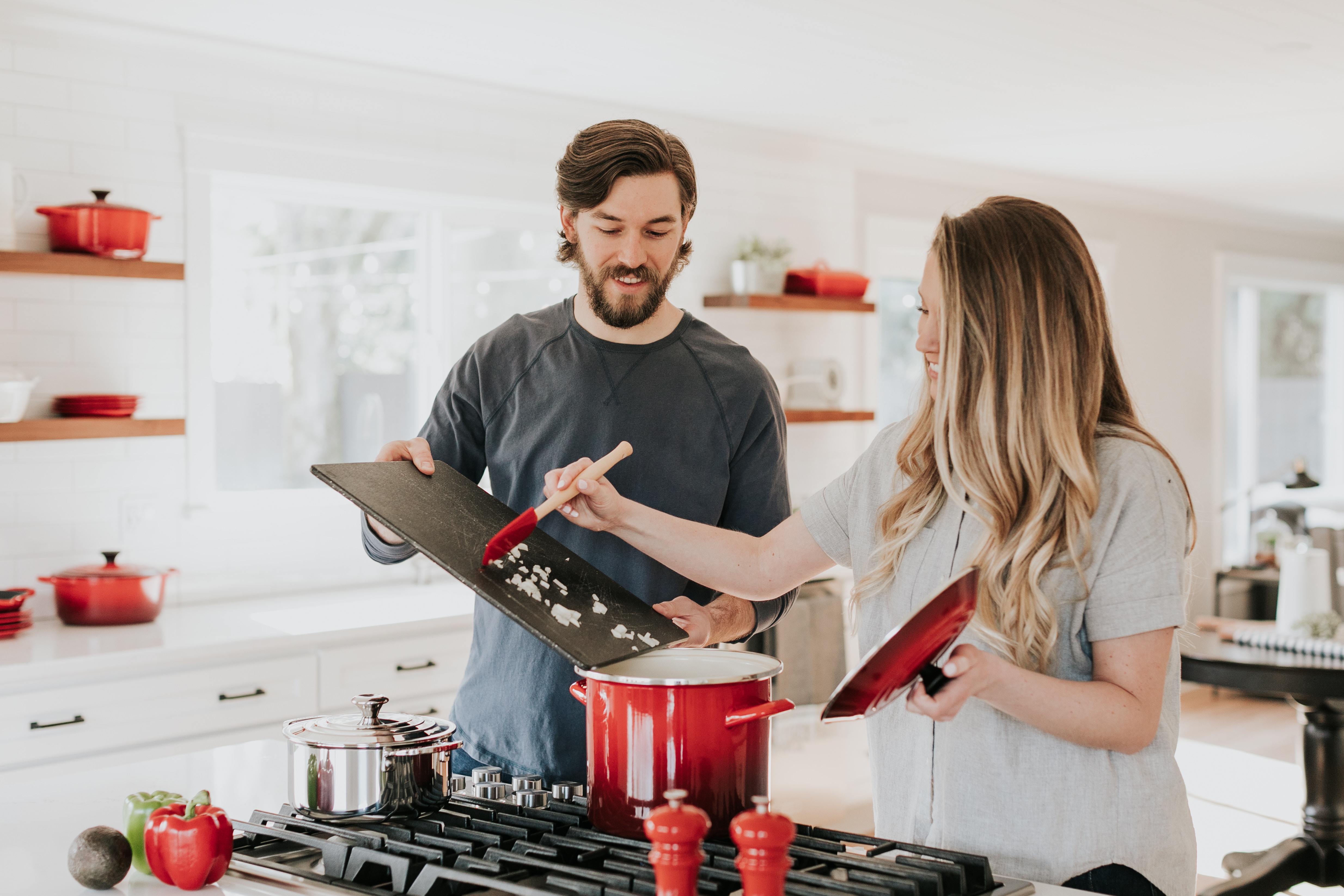 Man and woman at home in the kitchen, putting ingredients into a pot on the gas stove.