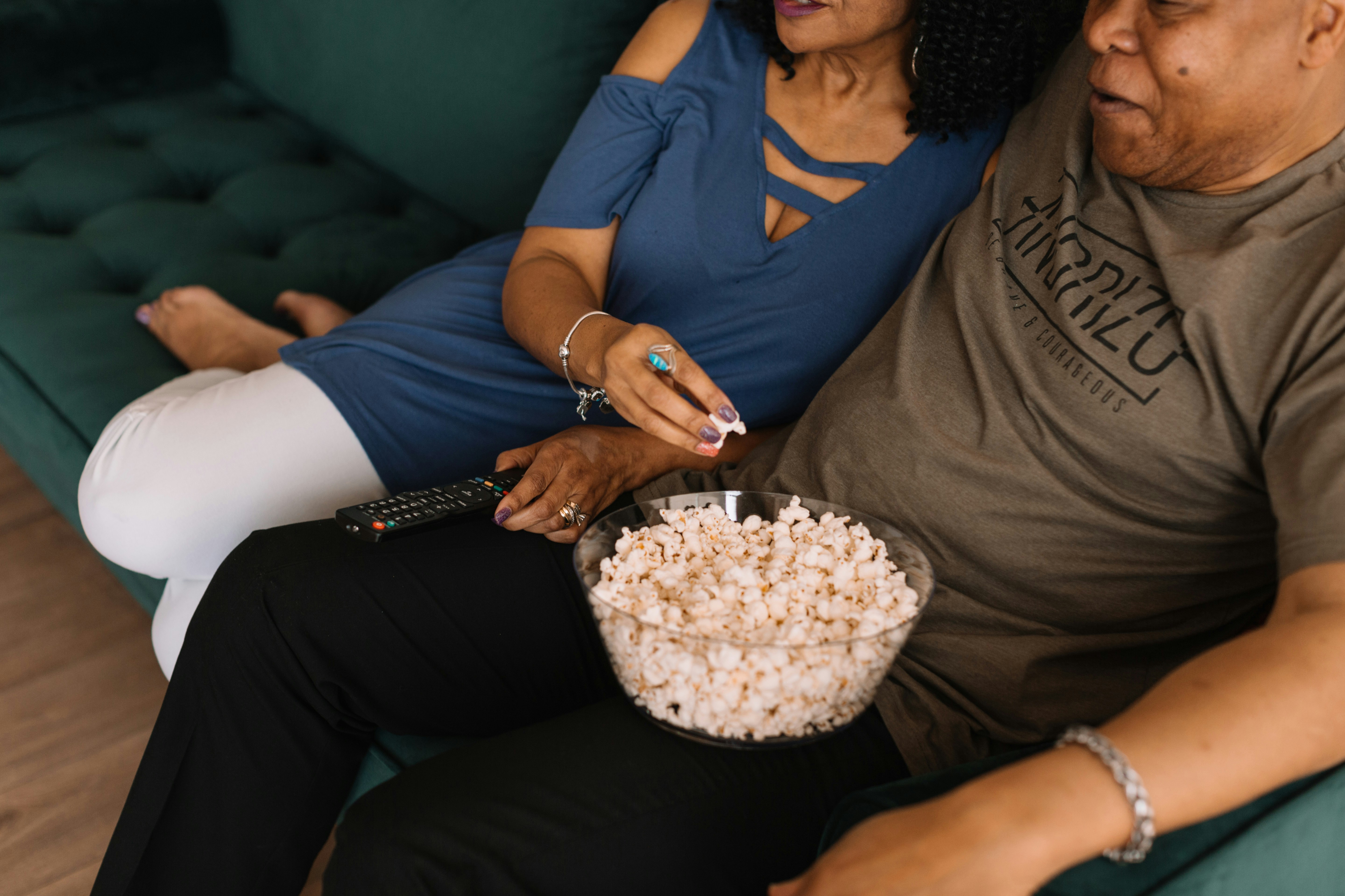 A couple sharing popcorn as they watch tv on the couch at home.