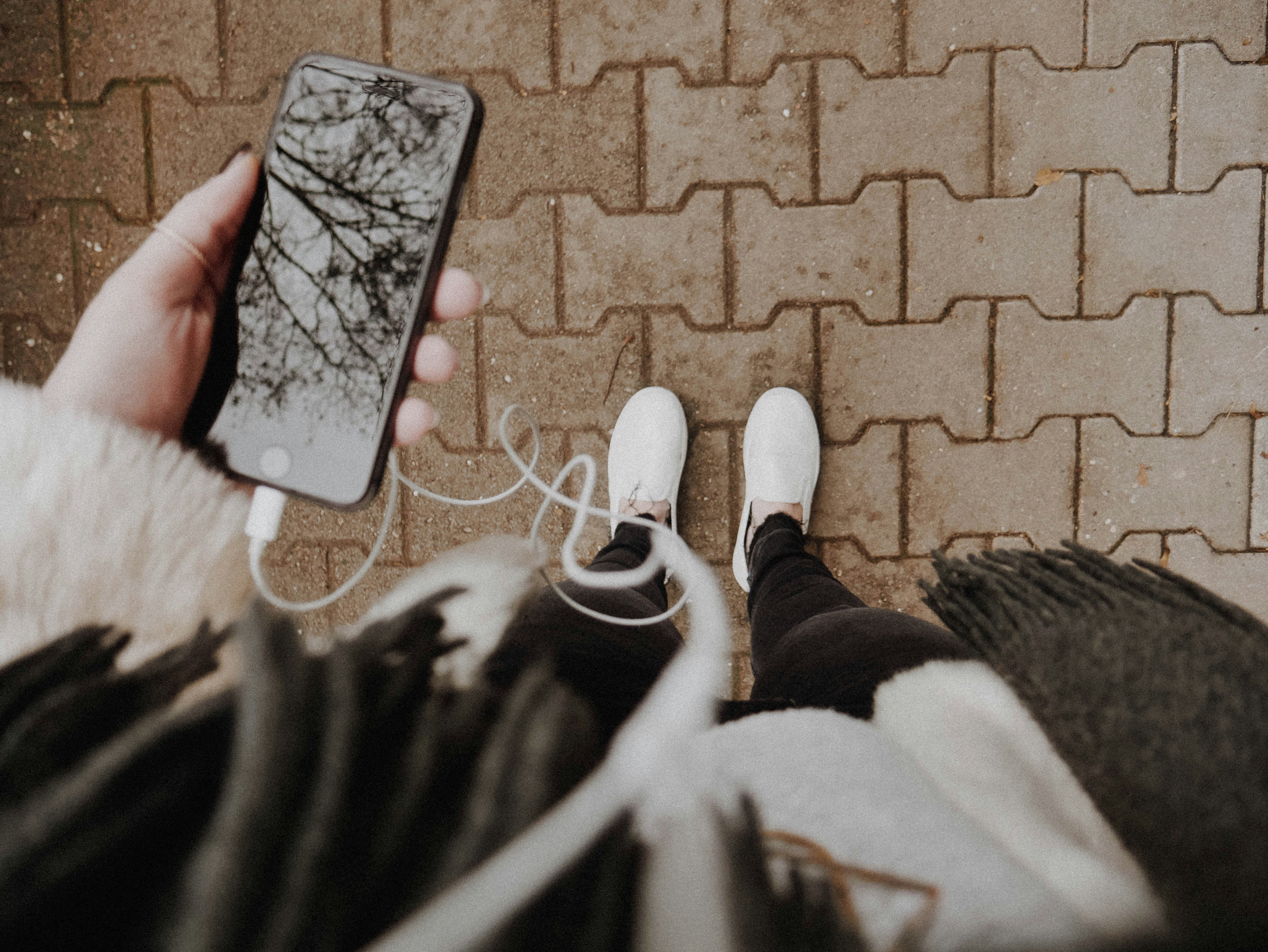 Woman holds her phone with headphones in to listen to a podcast while she walks or runs.