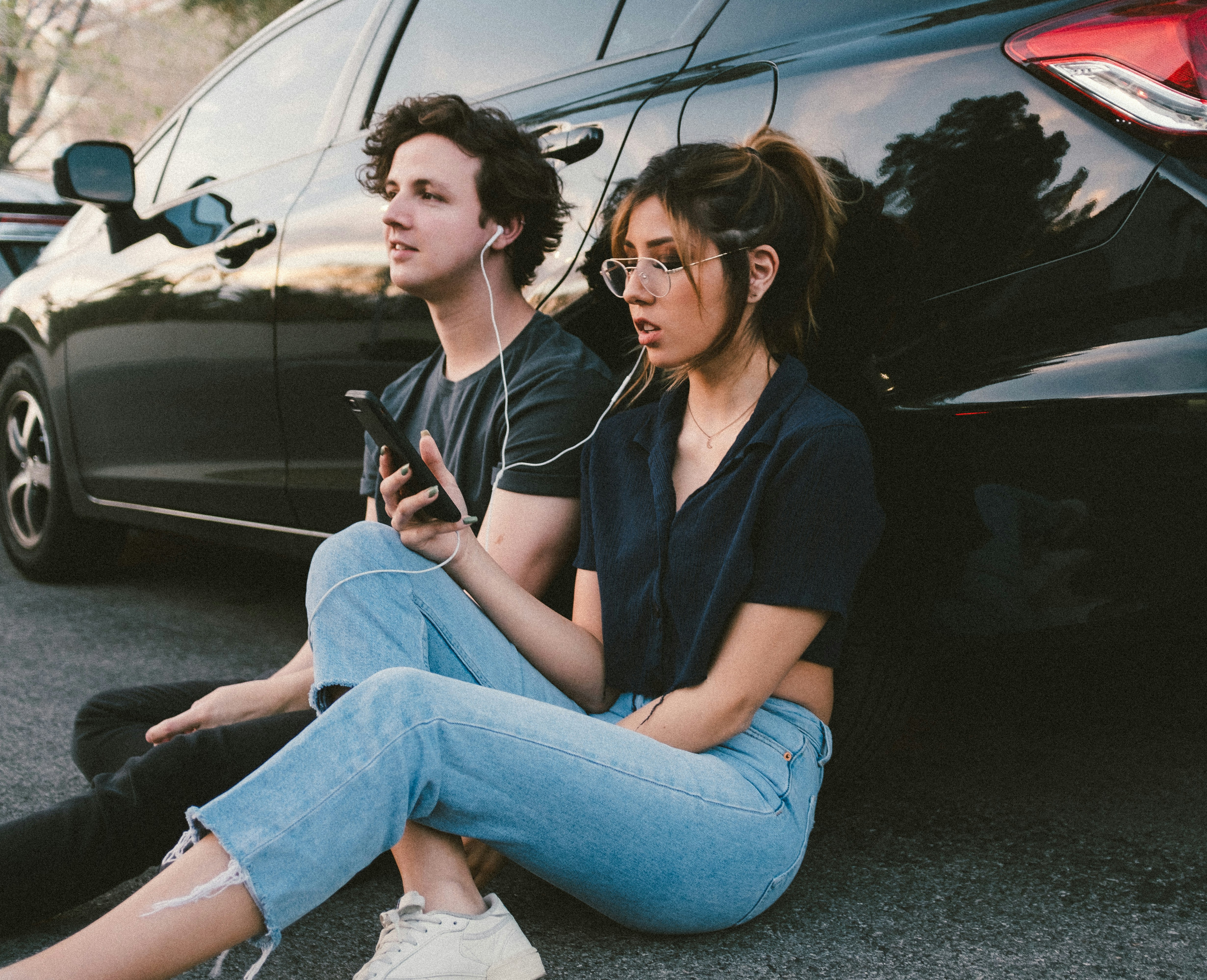 A man and woman share earbuds as they listen to a podcast on the woman's phone.