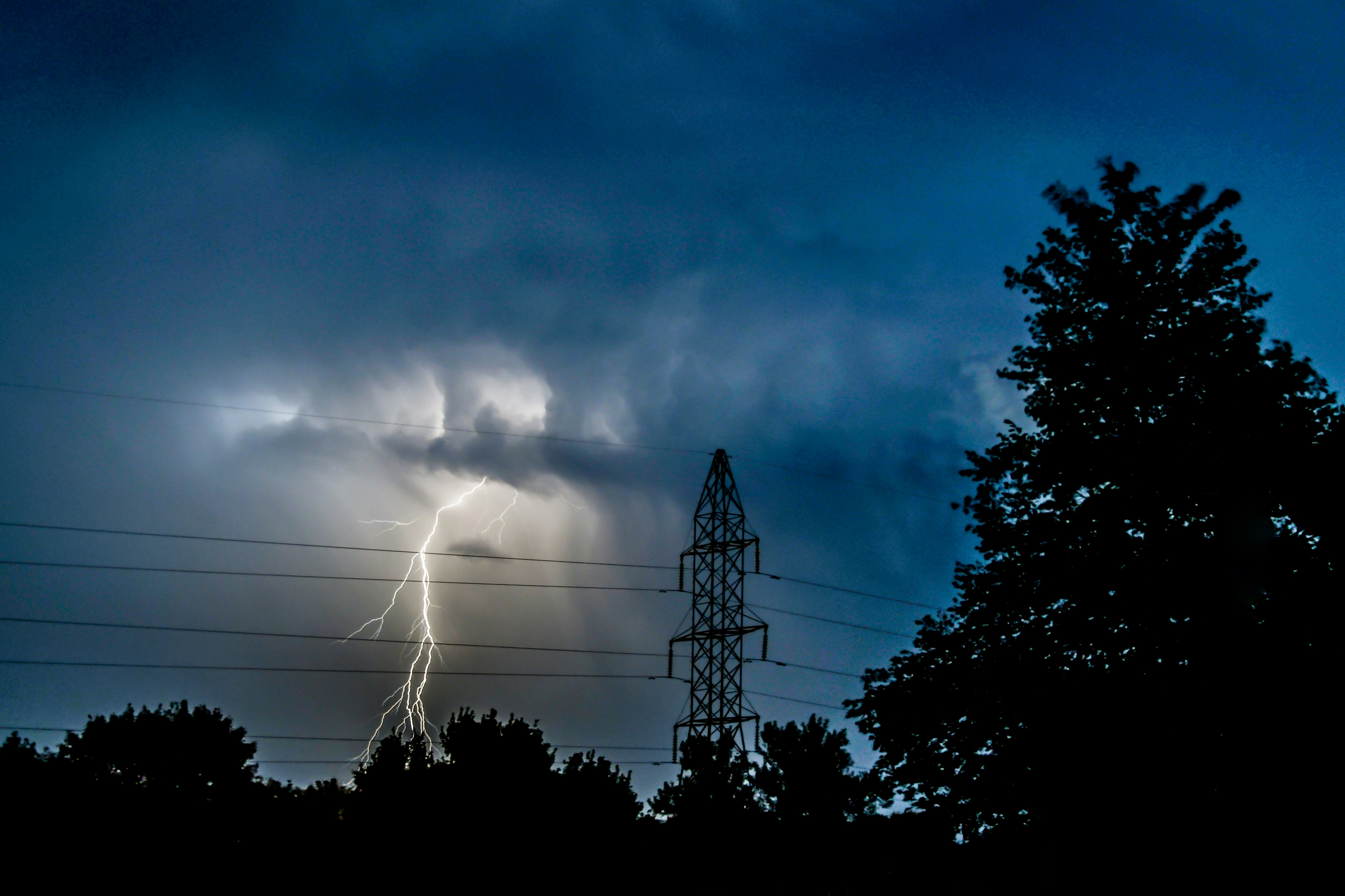 A bolt of lightning glowing behind power lines.