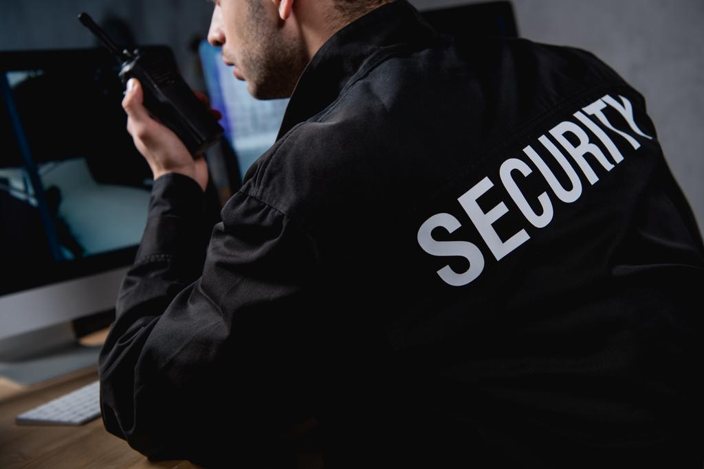 Security guard calls for backup on a walkie talkie while monitoring cameras.