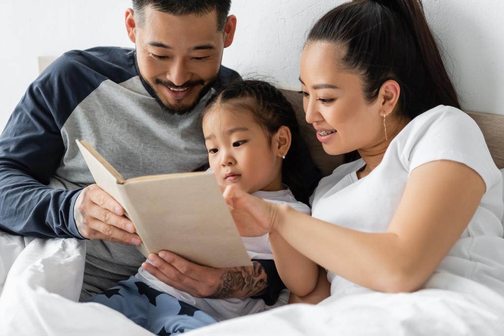 Mom and dad reading with their daughter in bed.