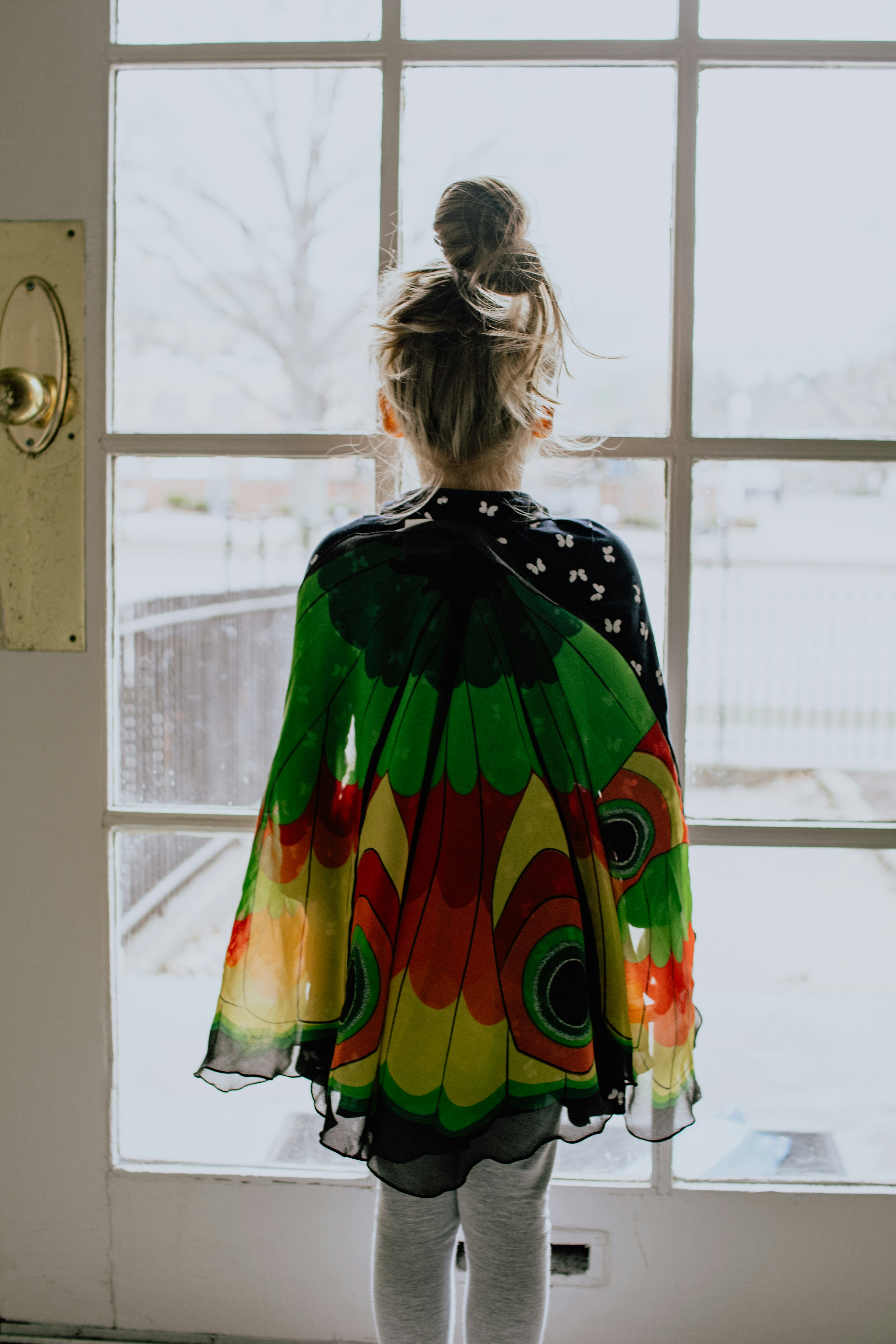 Young girl wearing wings standing in front of a door.