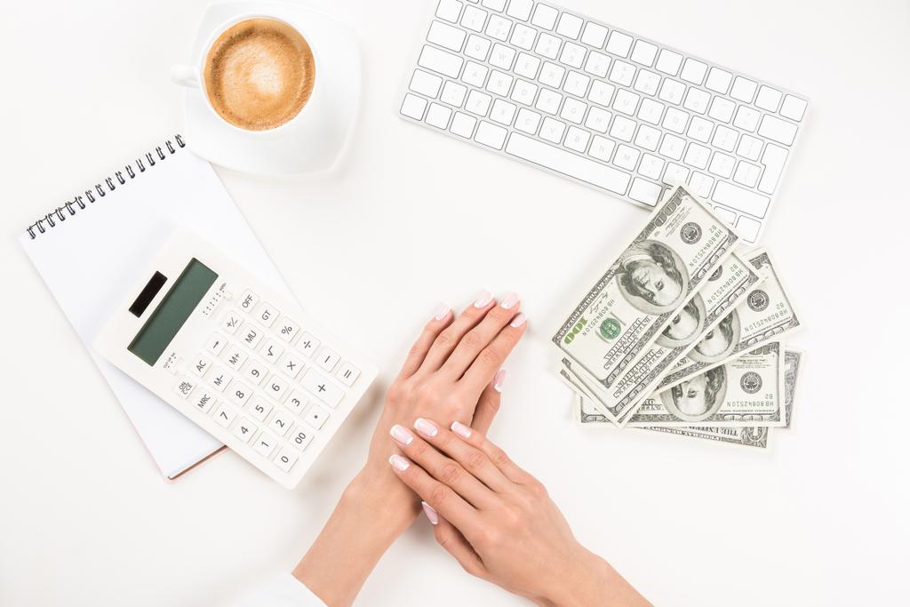 Desk with calculator, cash, keyboard, coffee, hands.